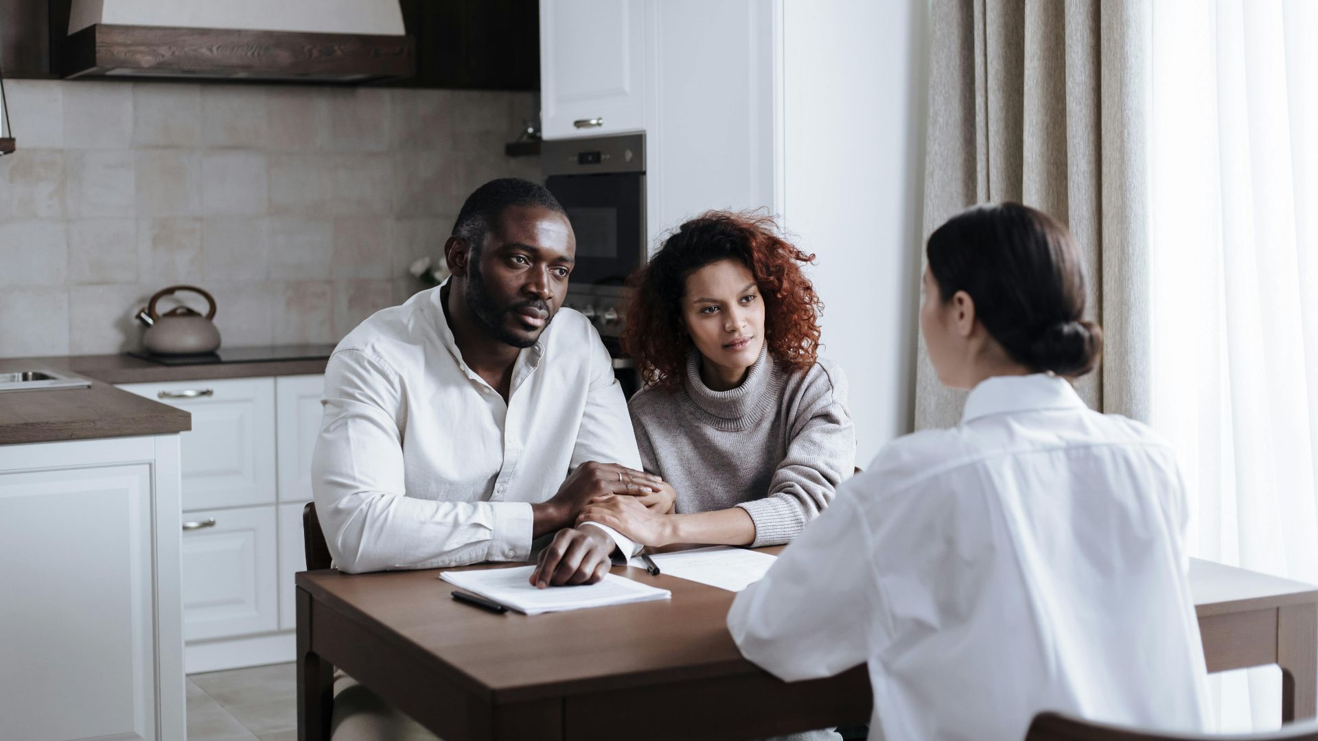 A couple discusses adoption with a social worker in a modern kitchen setting.