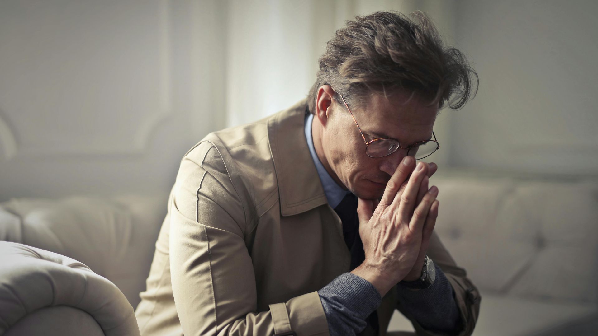 Side view of upset male entrepreneur in formal wear sitting on couch in modern living room and contemplating about financial problems while leaning on hands and looking down