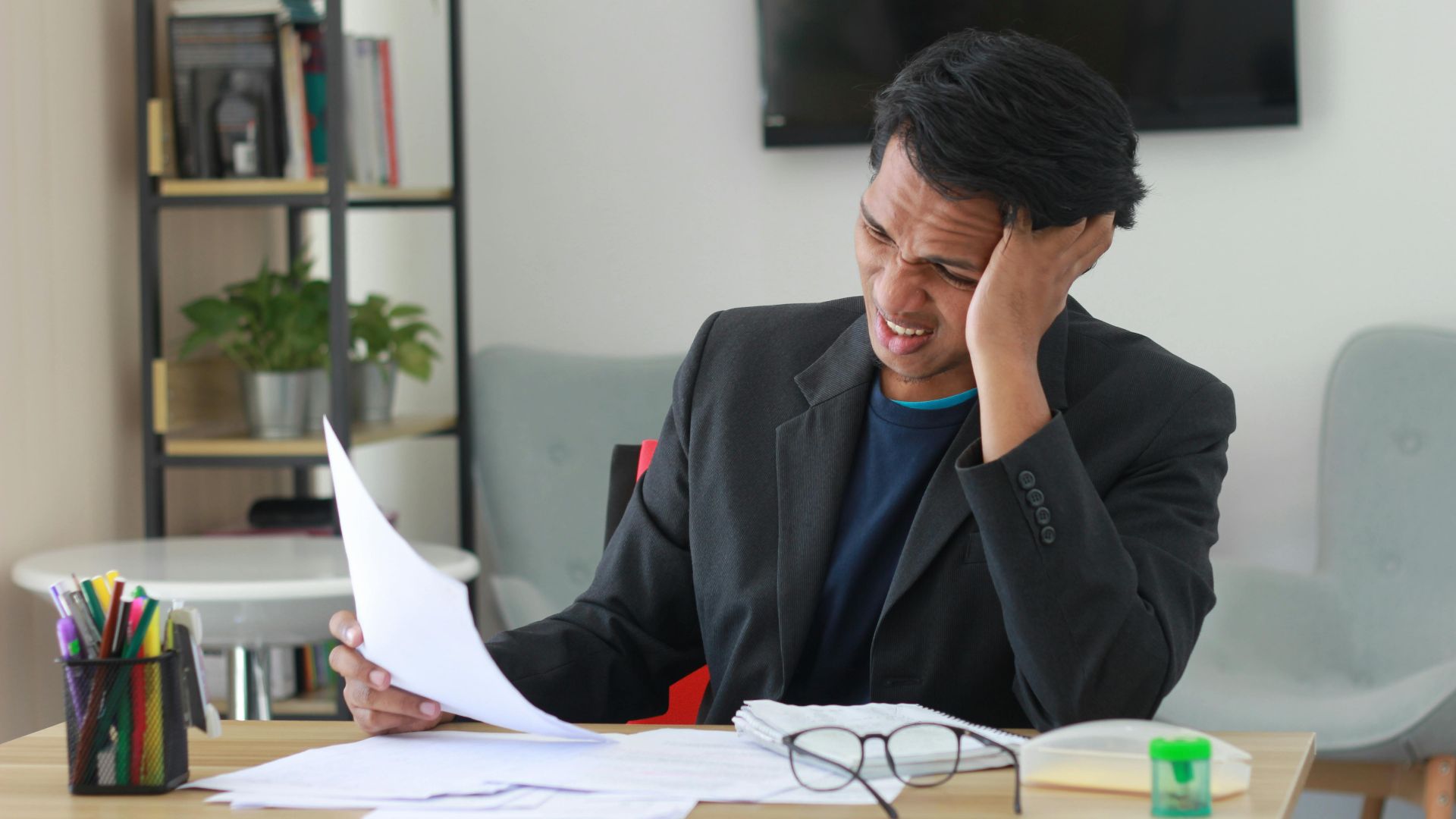 A businessman in an office experiencing stress while reviewing documents.