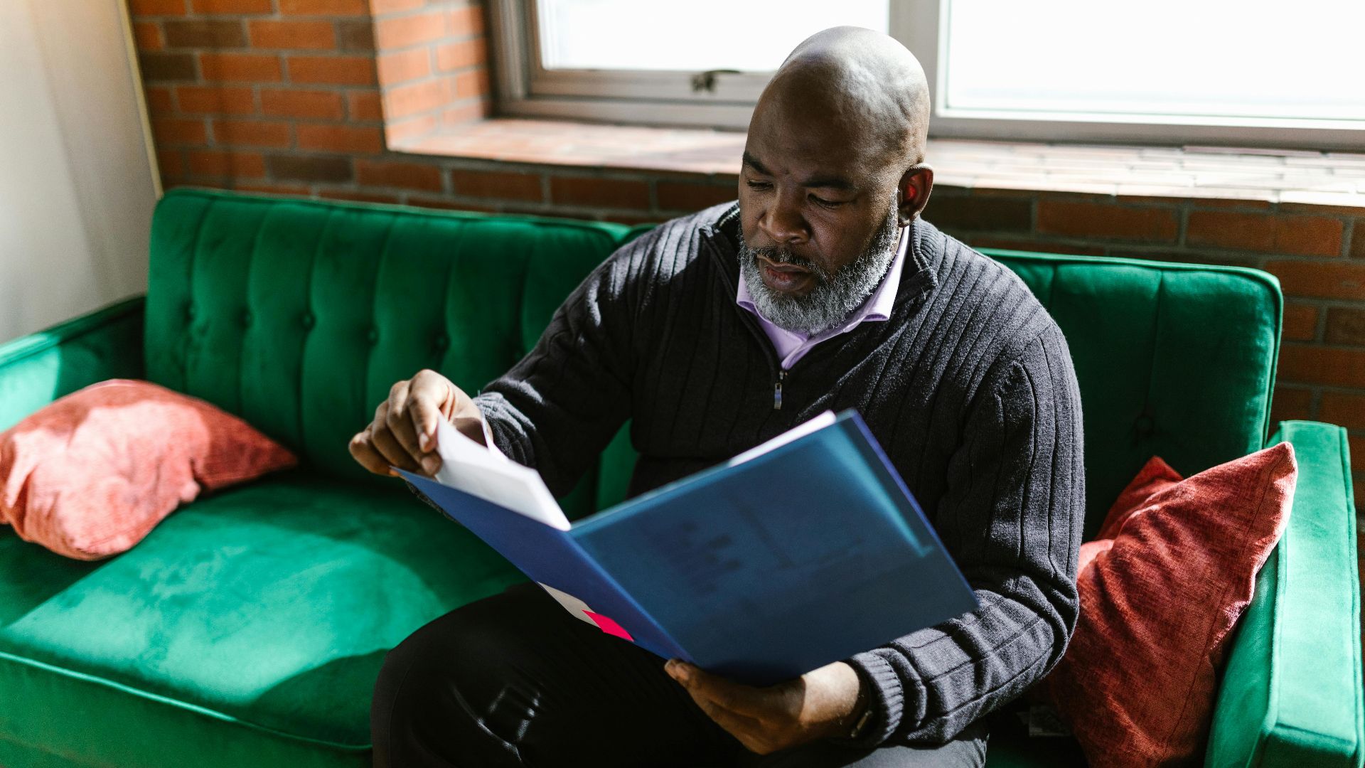 African American adult man reviewing documents on a green sofa, indoors.