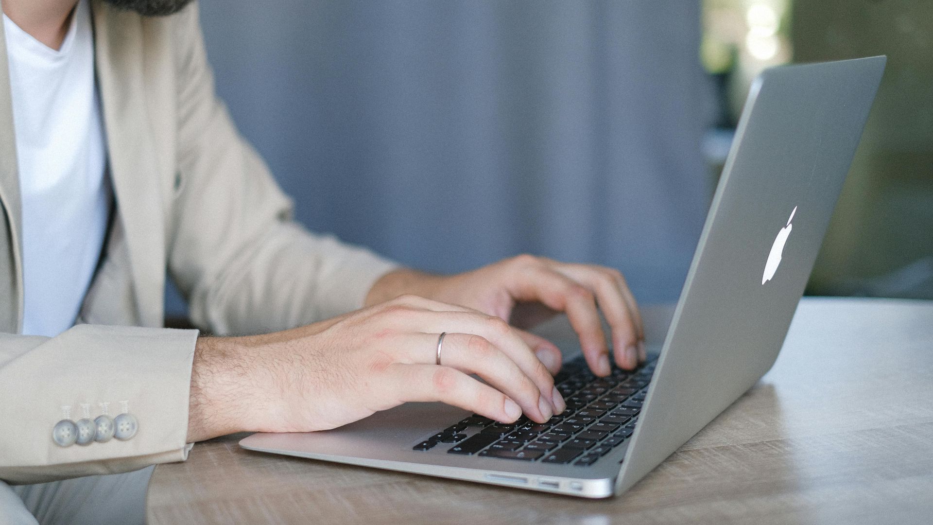 Side view of crop bearded male entrepreneur wearing classy jacket sitting at wooden table and browsing modern netbook in daylight