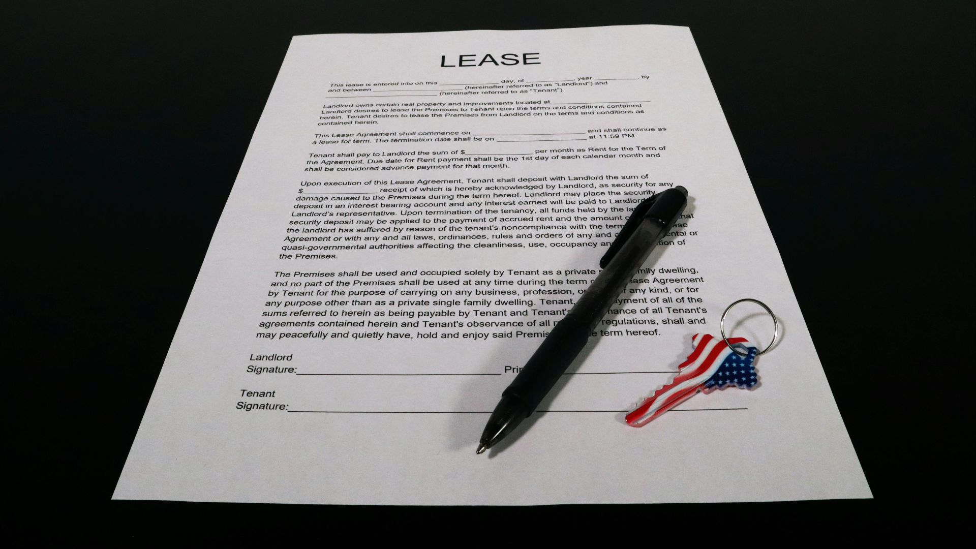 Lease agreement document with pen and American flag keychain on a black table.