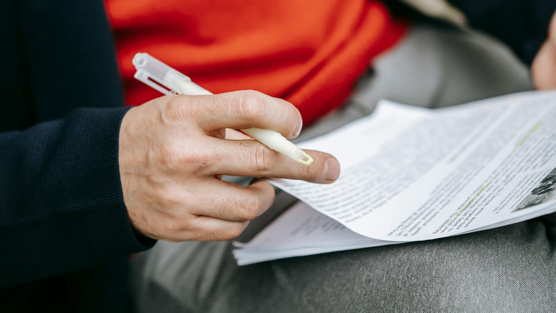 A focused individual reviewing documents outdoors, pen in hand, wearing vibrant clothing.