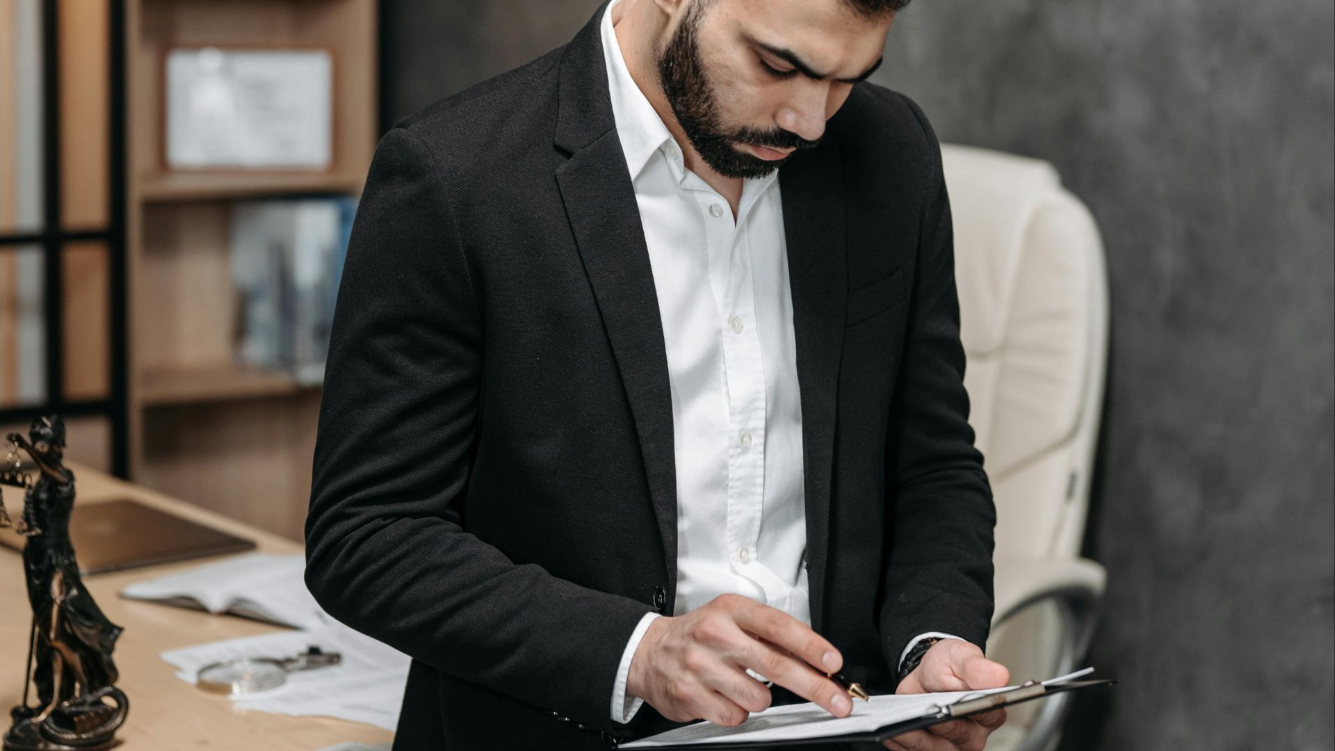 Focused male in suit reviewing paperwork in modern office setting.