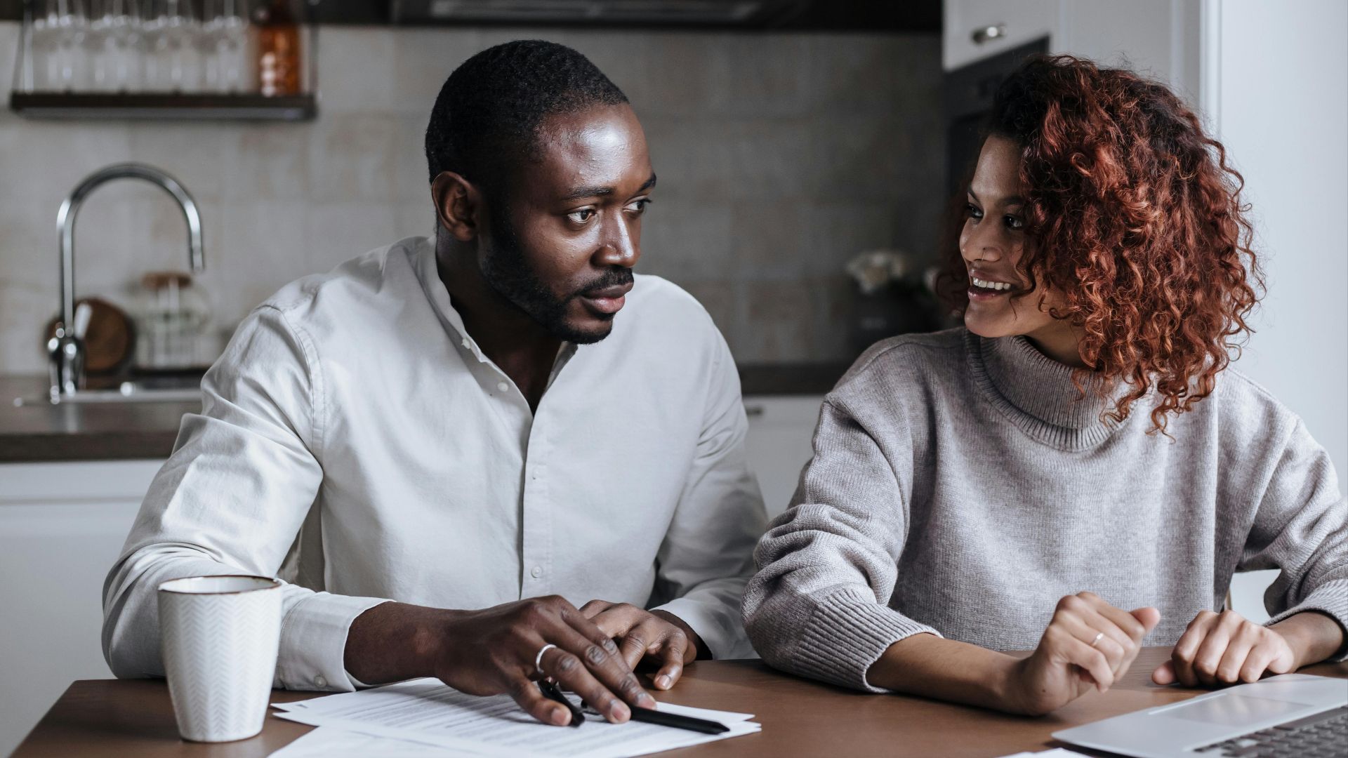 Black couple collaborating on a project at their kitchen table, showcasing teamwork and home office lifestyle.