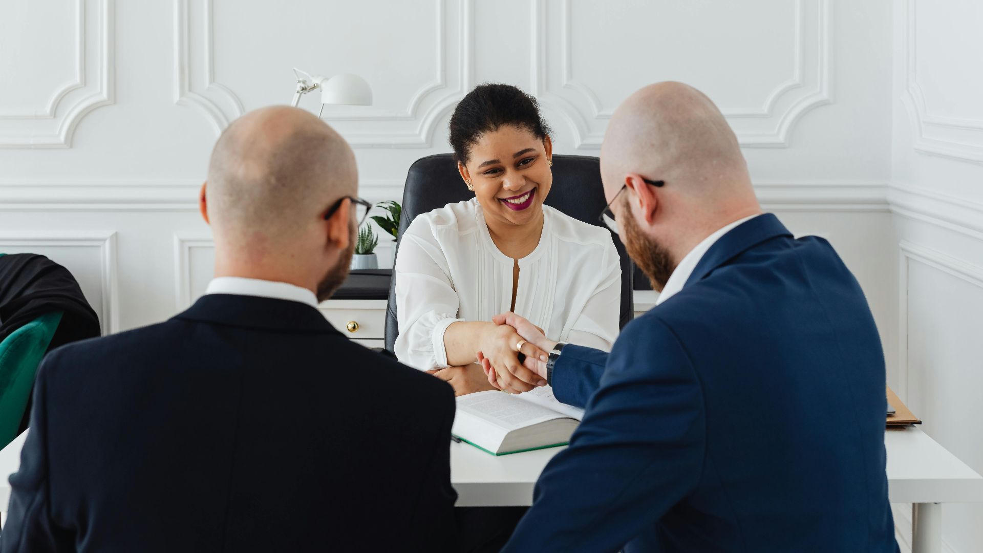 Diverse professionals in a business meeting, shaking hands across a table, indoors.