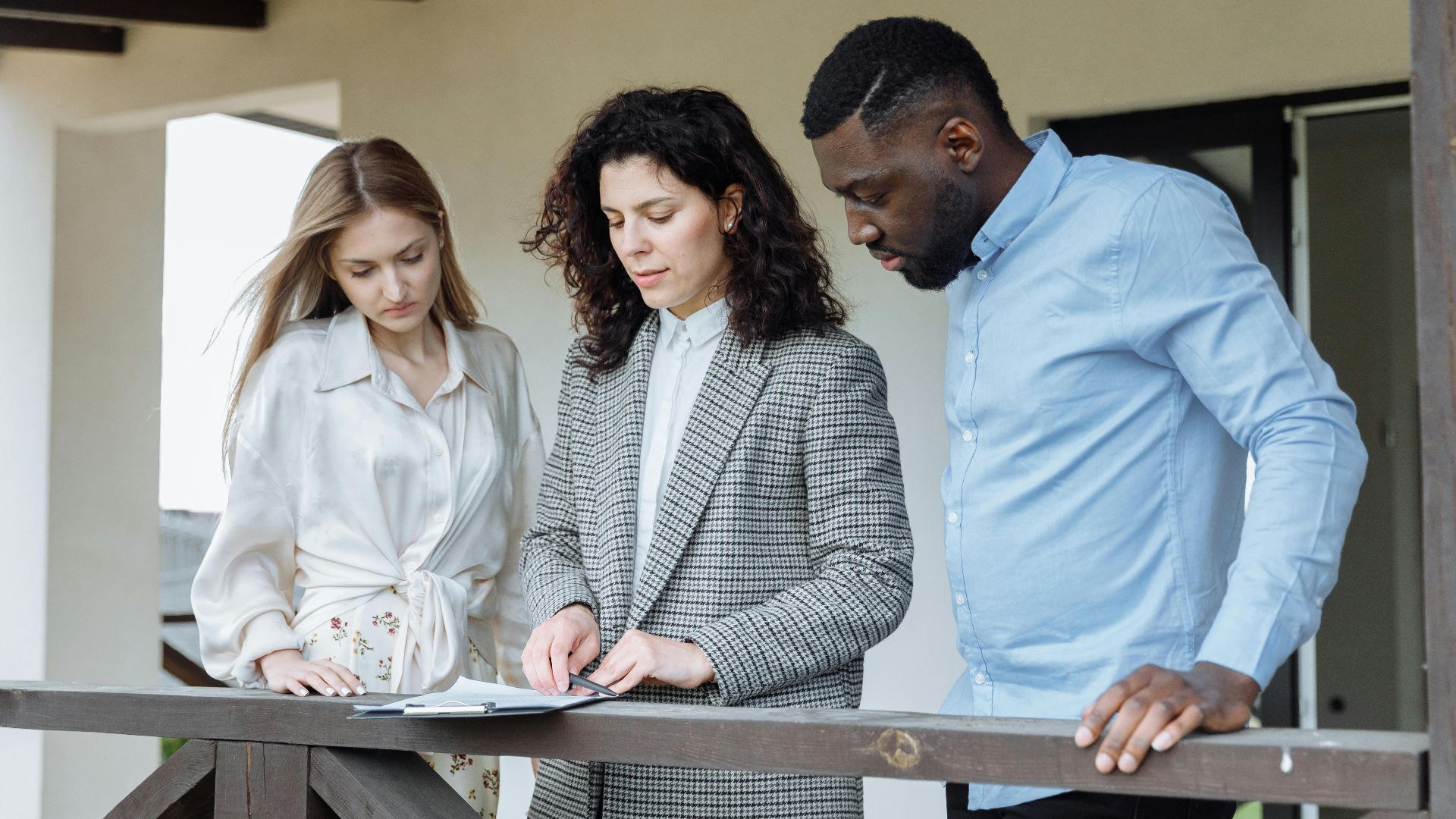 Three adults reviewing documents on a balcony during a real estate consultation.