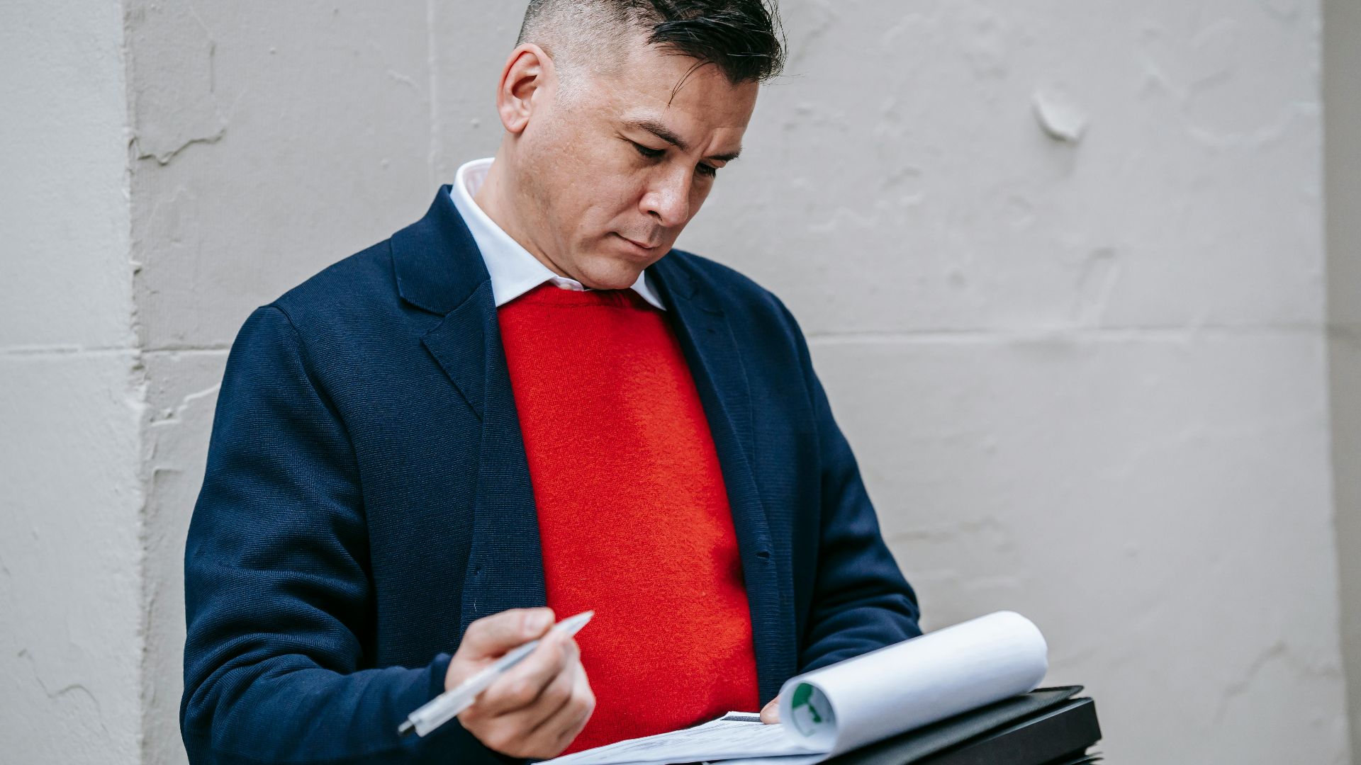 A focused professional man in stylish attire writing notes on paper outside.