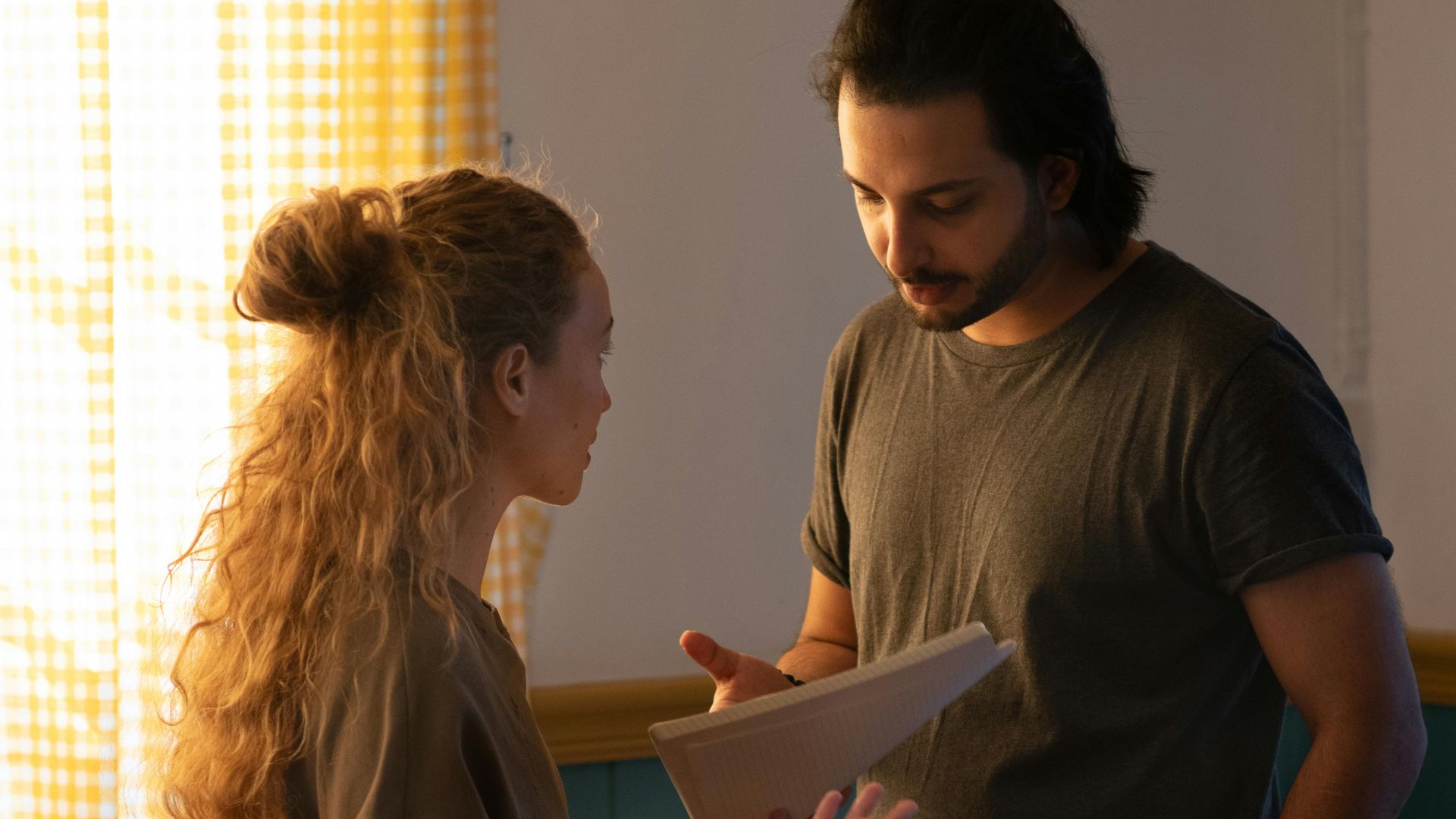 Concentrated couple talking to each other standing in room of new apartment with moved items while woman holding paper sheets and man pointing at paper putting hand in pocket