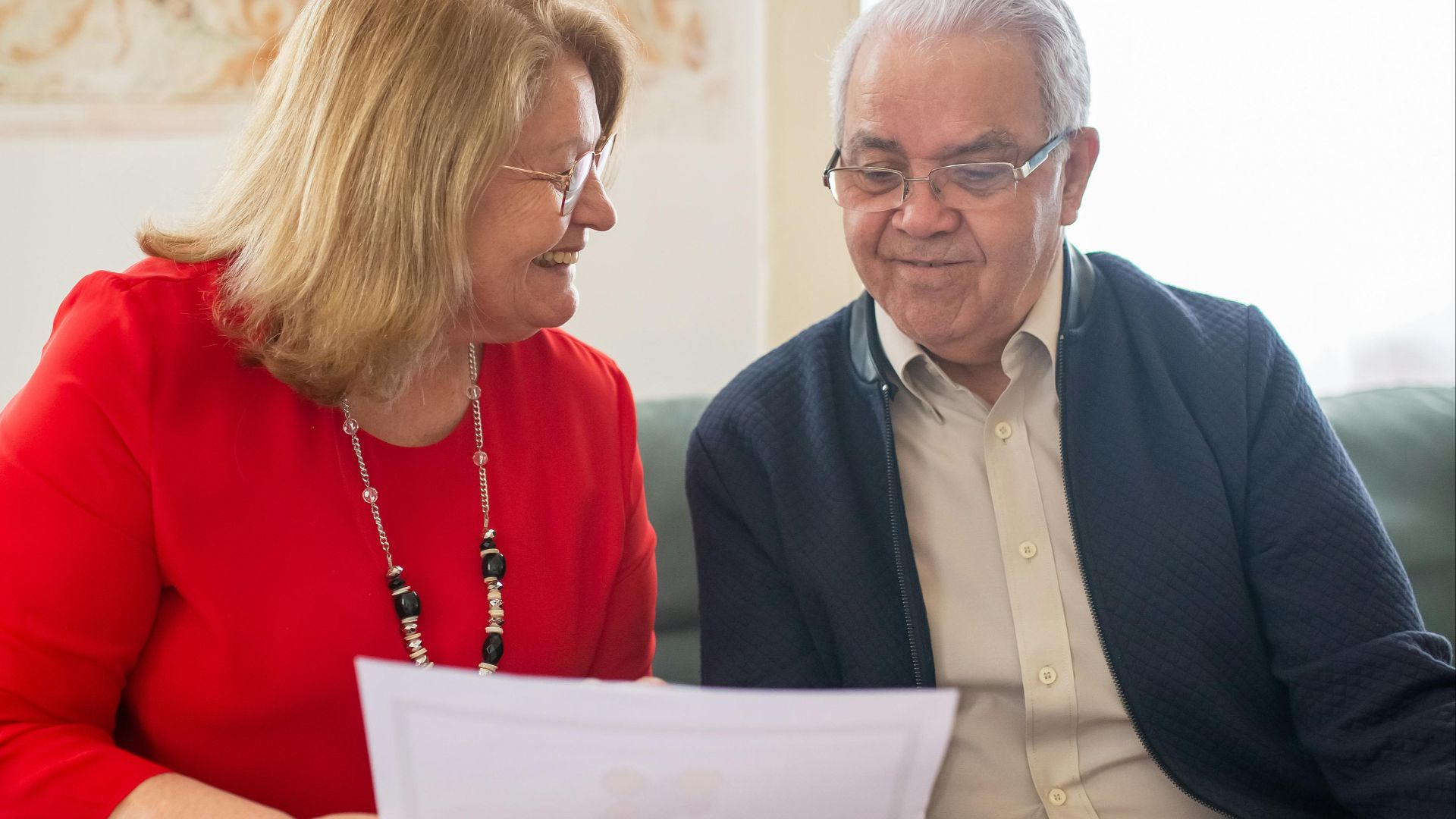 Senior couple consulting on pension options, smiling on a sofa, discussing documents.