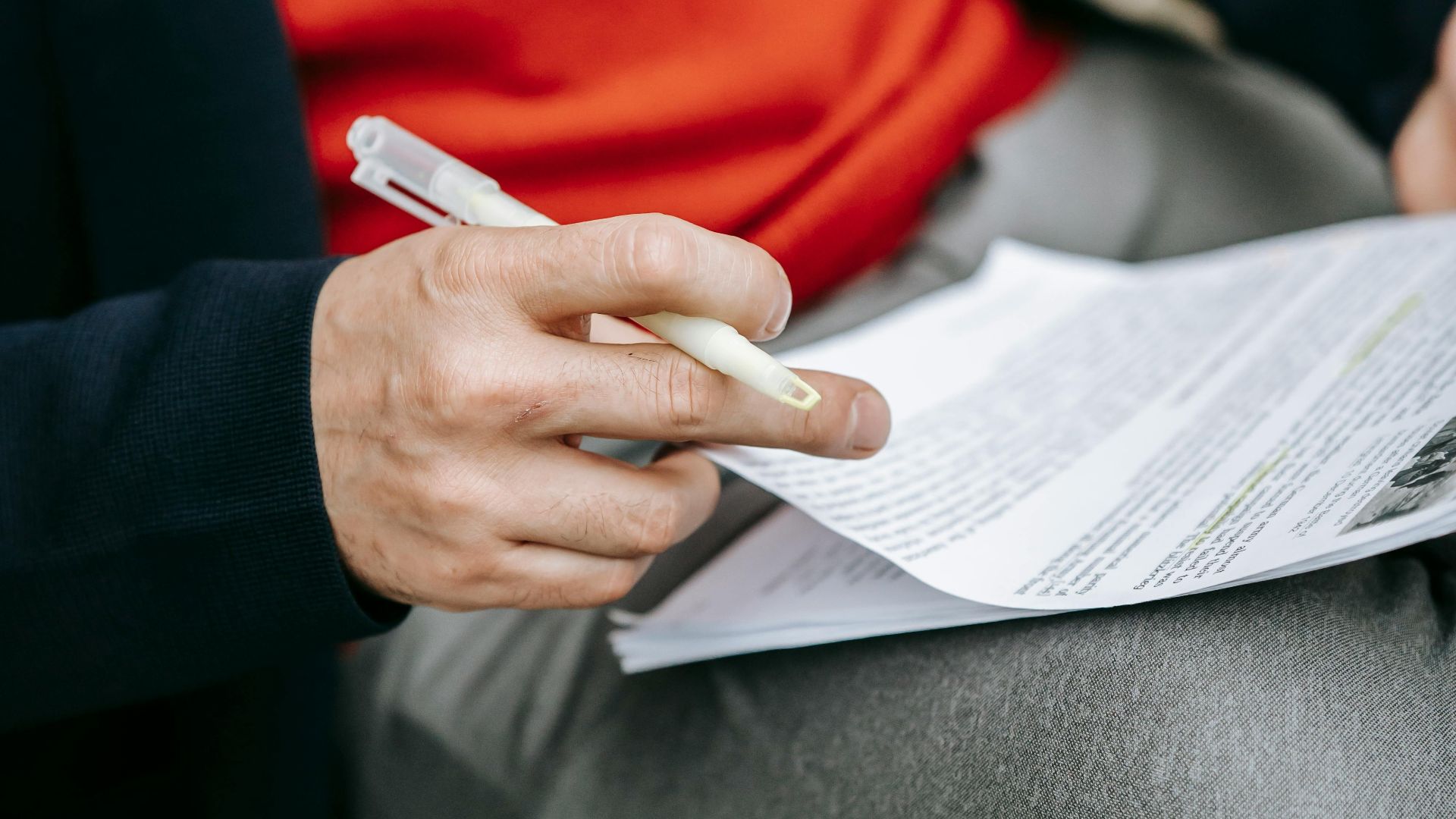 A focused individual reviewing documents outdoors, pen in hand, wearing vibrant clothing.