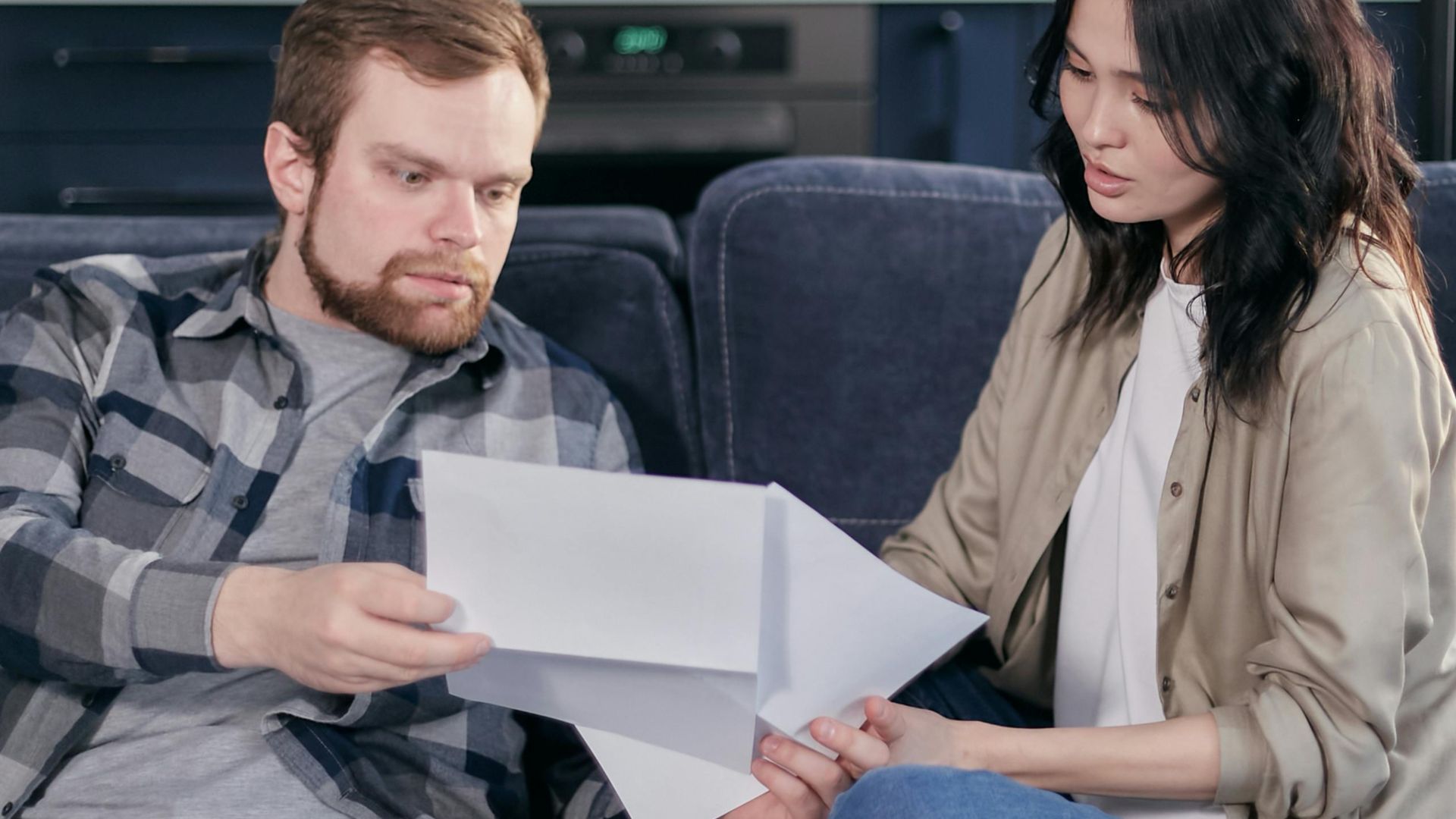 Asian woman and Caucasian man discussing taxes on couch.