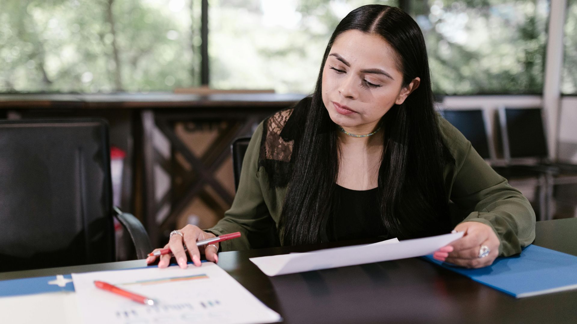 Professional woman in office setting studying documents with concentration.