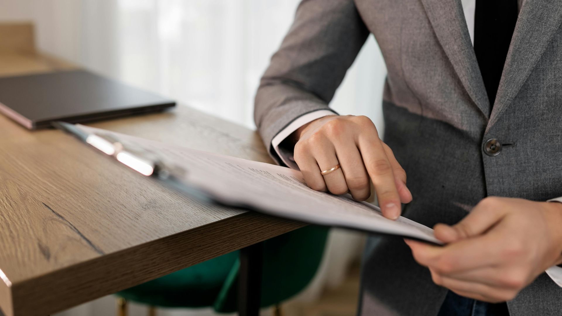 Professional businessman in suit reviewing documents on clipboard at office desk.
