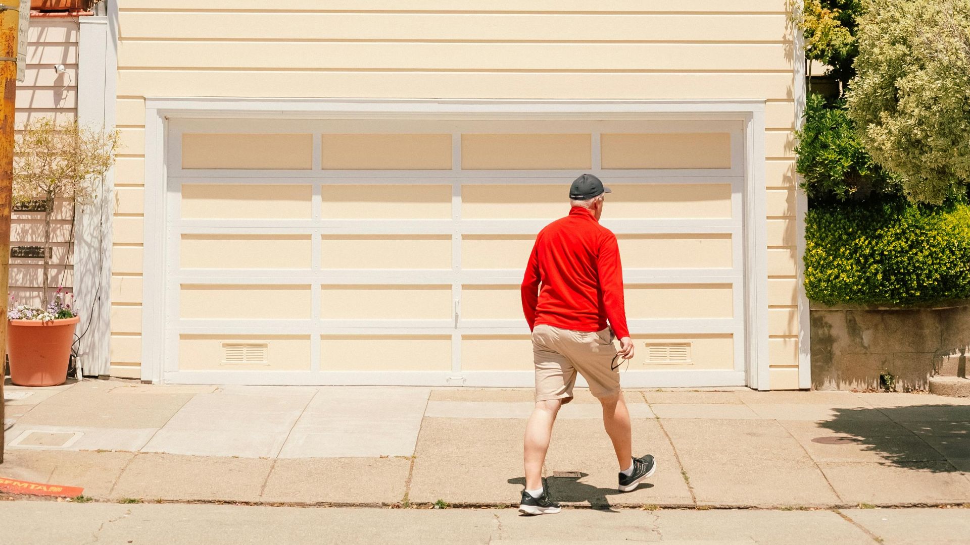 A man walks by a sunlit Victorian house in an urban neighborhood.