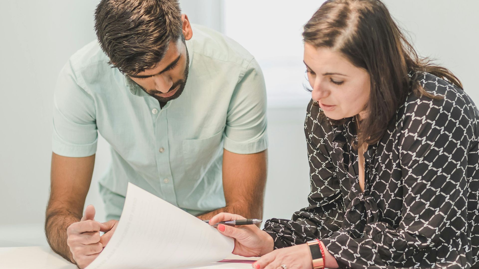 Real estate agent assisting first-time homebuyer with documents inside a bright room.
