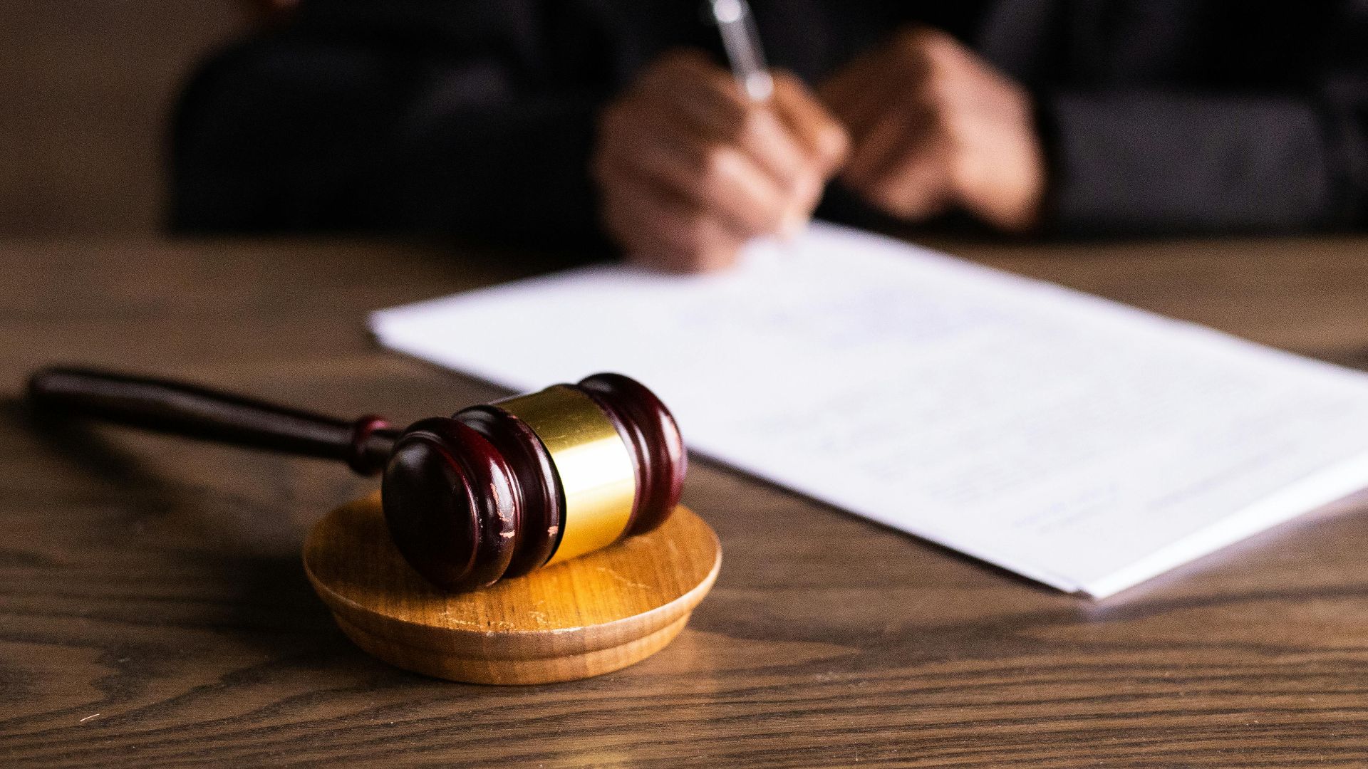 Judge signing documents at desk with focus on gavel, representing law and justice.