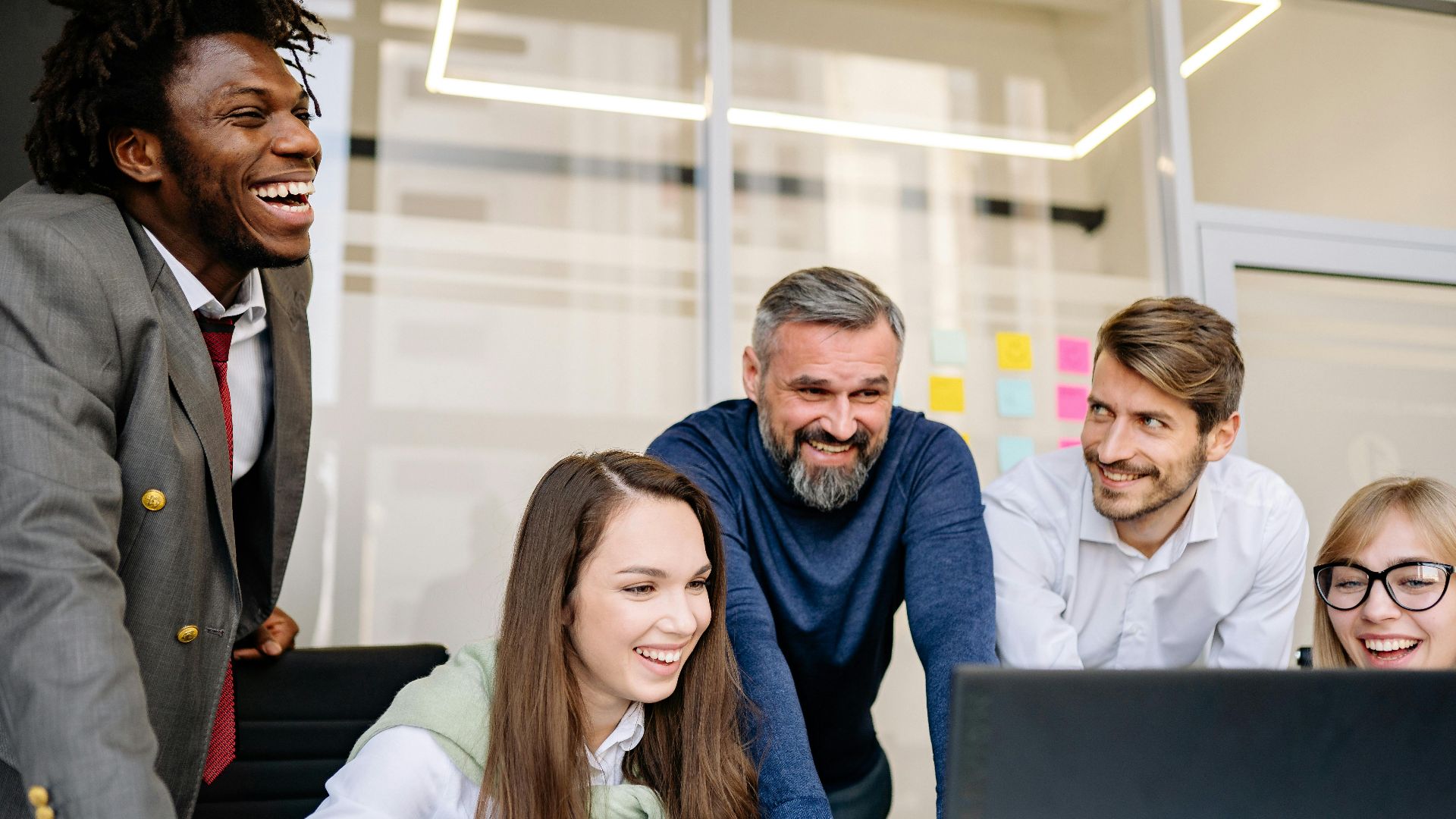 A diverse group of colleagues enthusiastically collaborating on a project in a brightly lit modern office.