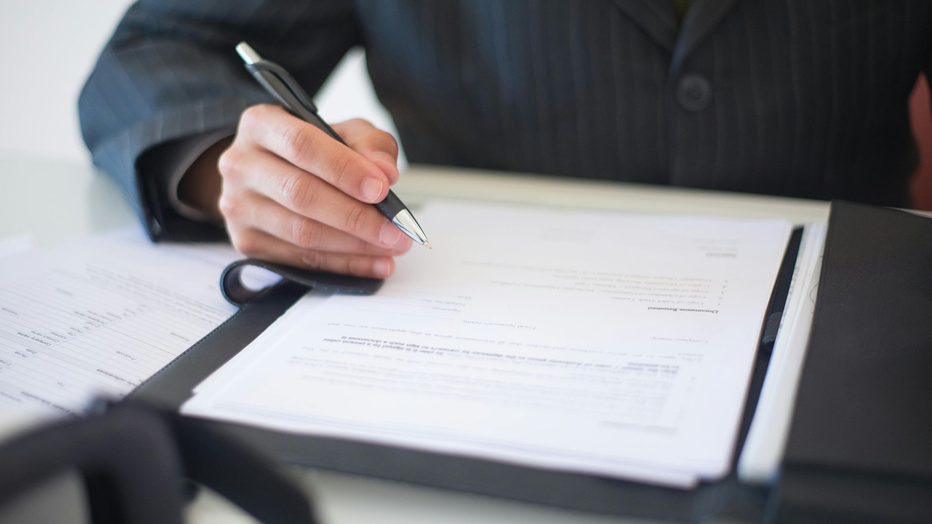 Close-up of a hand signing documents with a pen, symbolizing an important business contract.