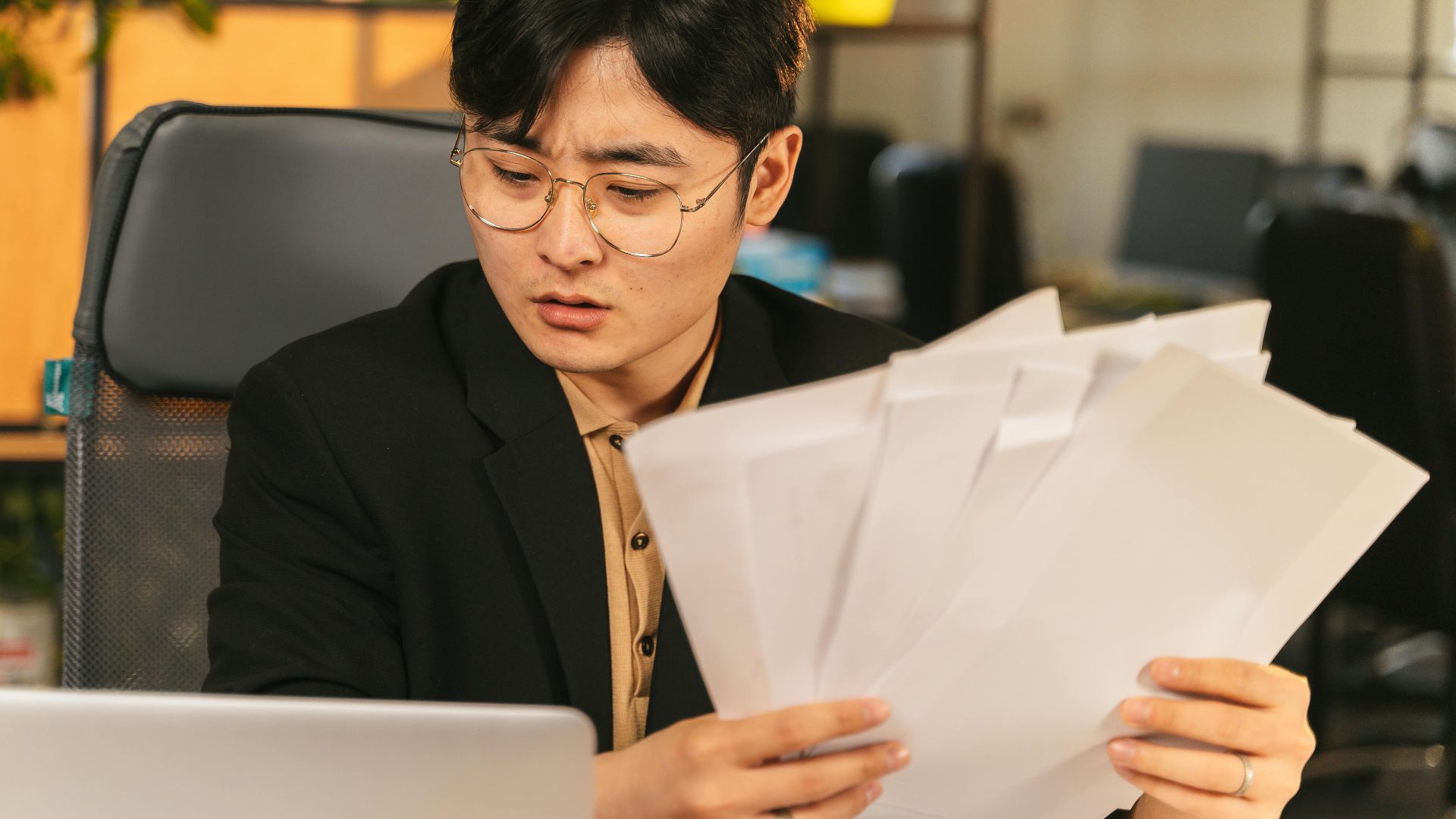 Businessman in glasses reviewing paperwork in a modern office setting.