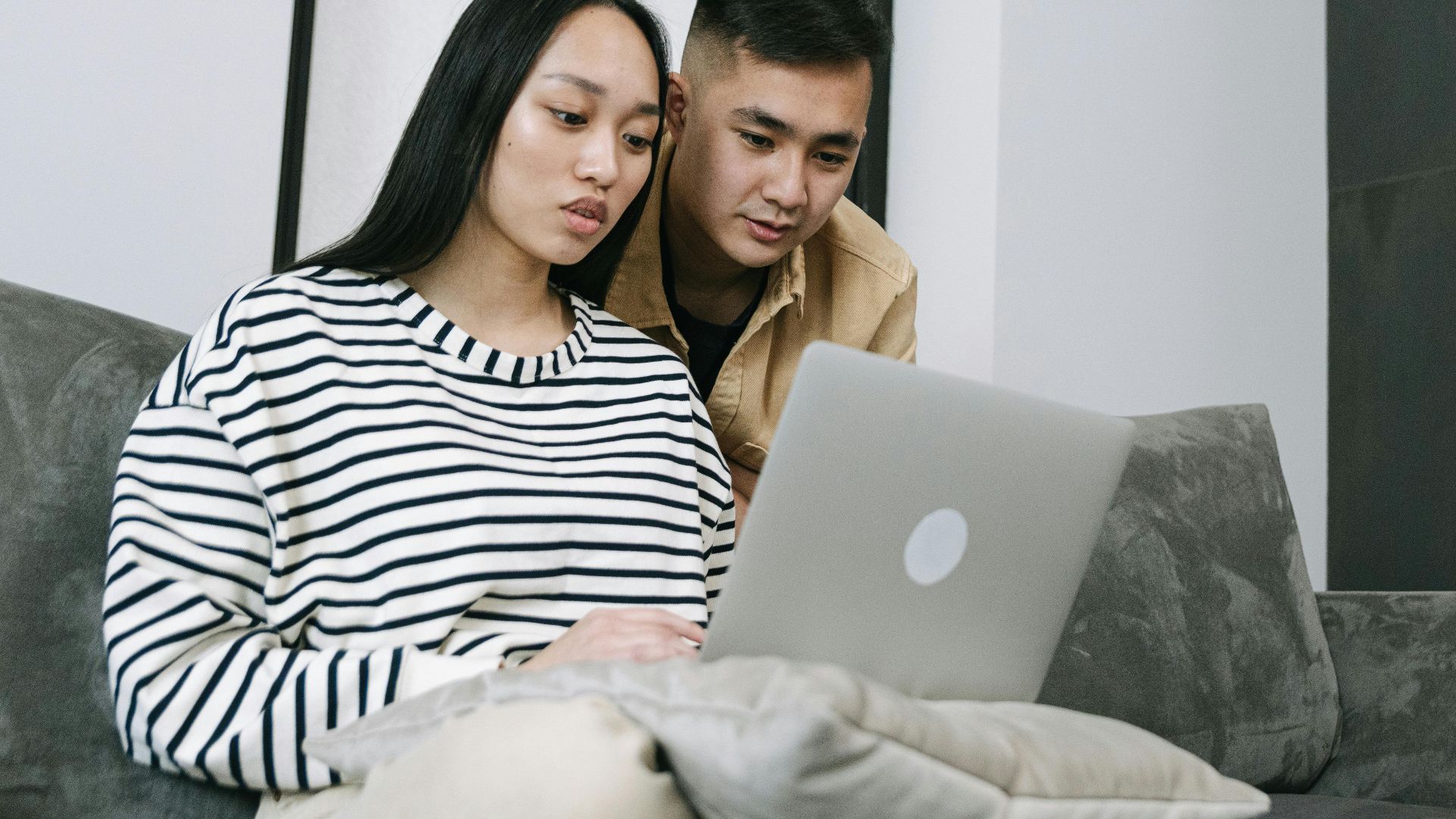 Young couple seated on sofa using laptop together in modern living room.