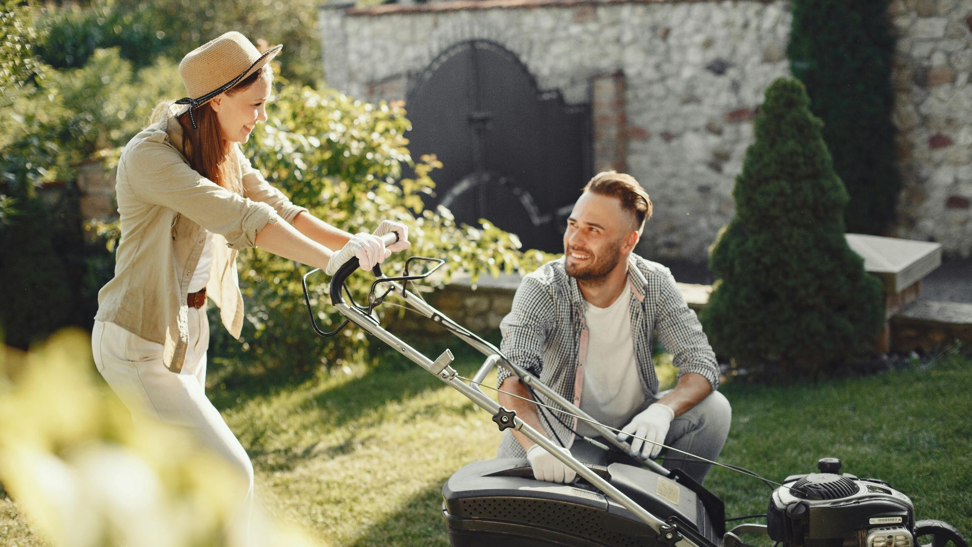 A cheerful couple working together in a garden with a lawn mower.