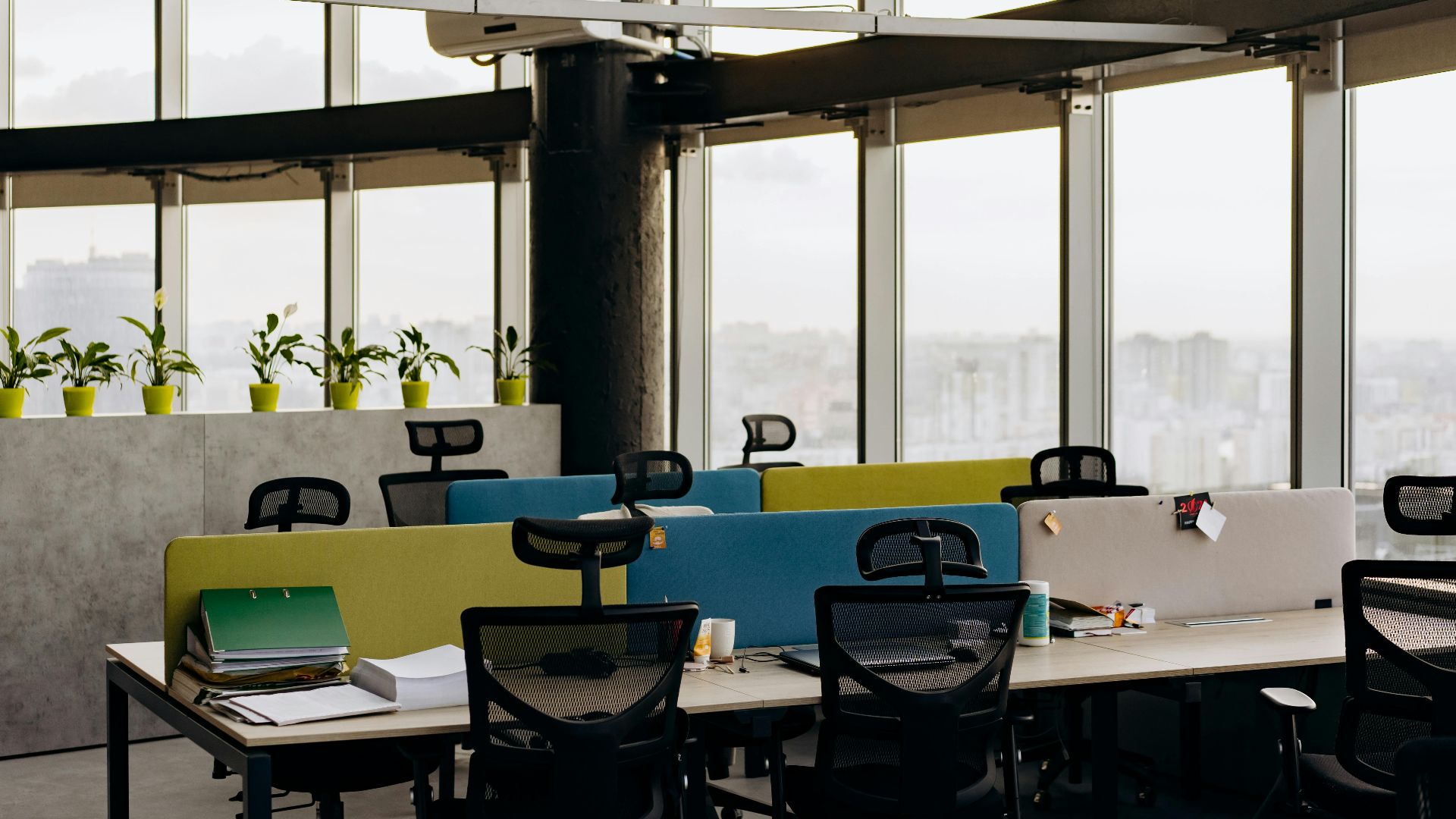 A spacious open office with colorful dividers, large windows, and a cityscape view, perfect for creative work environments.