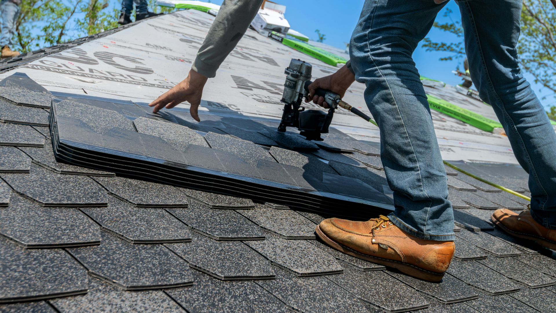 Roofer using nail gun for shingle installation on residential roof.