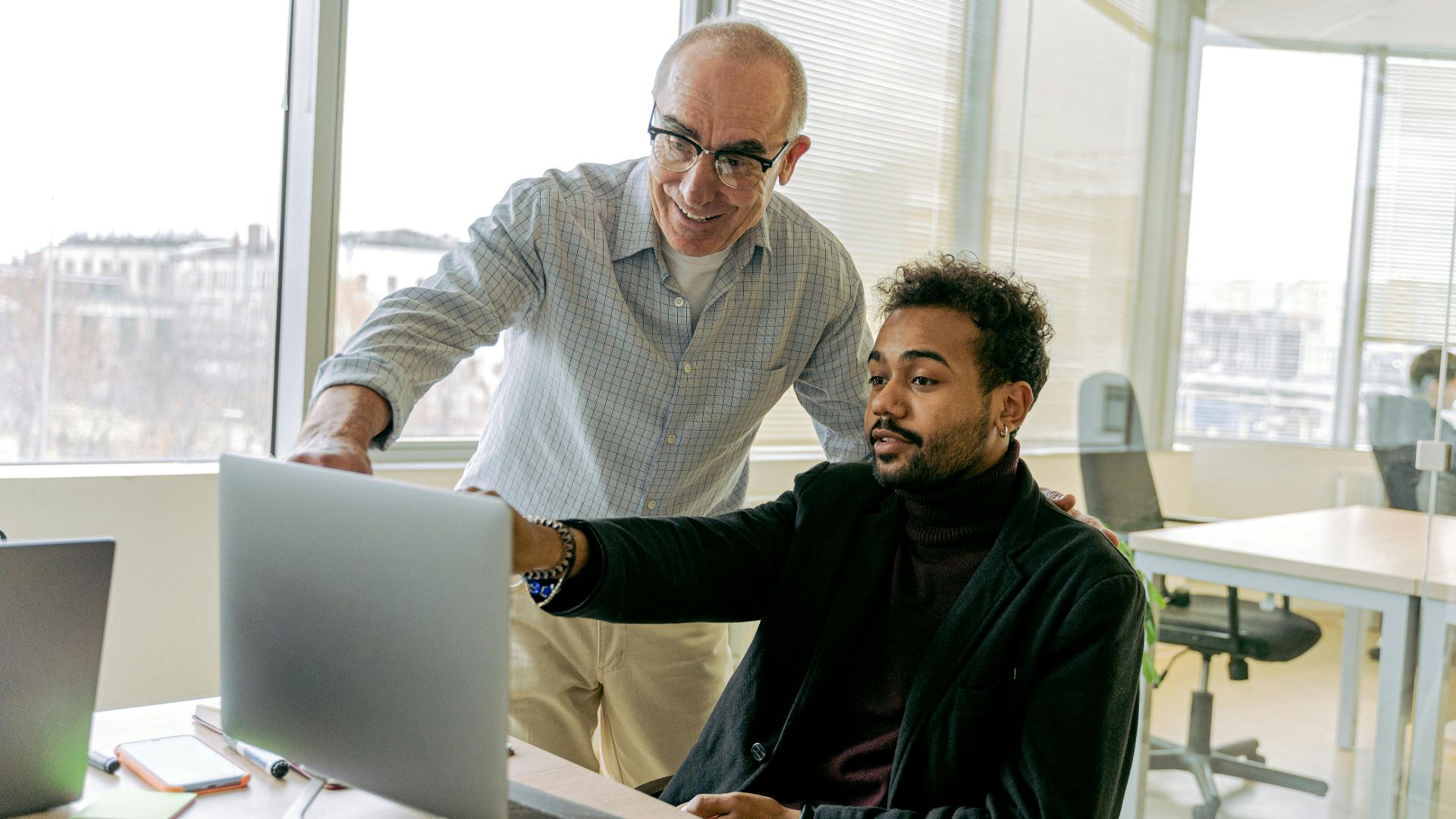 Colleagues collaborating in a bright office environment, focusing on a laptop screen.
