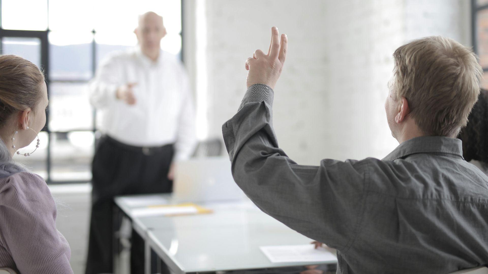 Back view of male worker in casual wear raising hand for asking question during corporate diverse group meeting in modern contemporary office boardroom