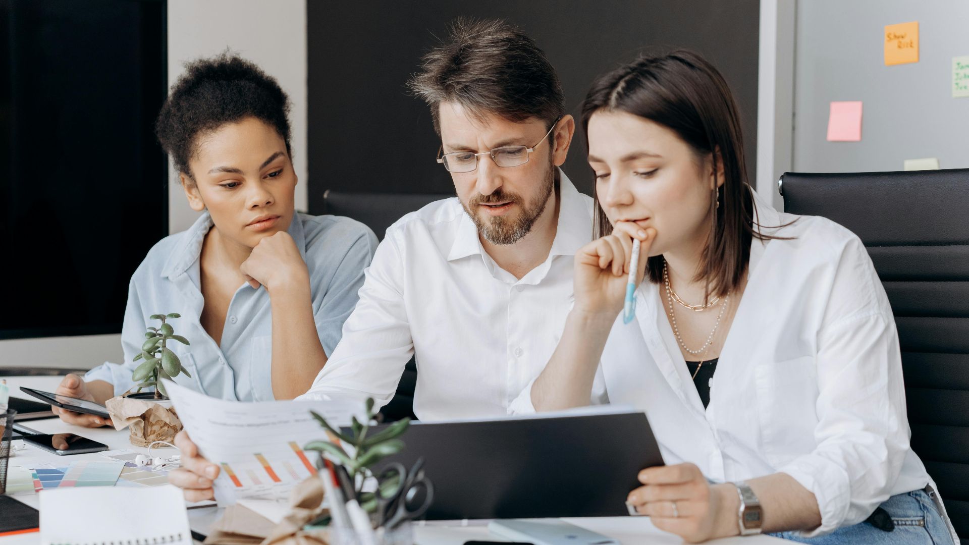 Three coworkers collaborating on a project at a modern office desk with charts and laptops.
