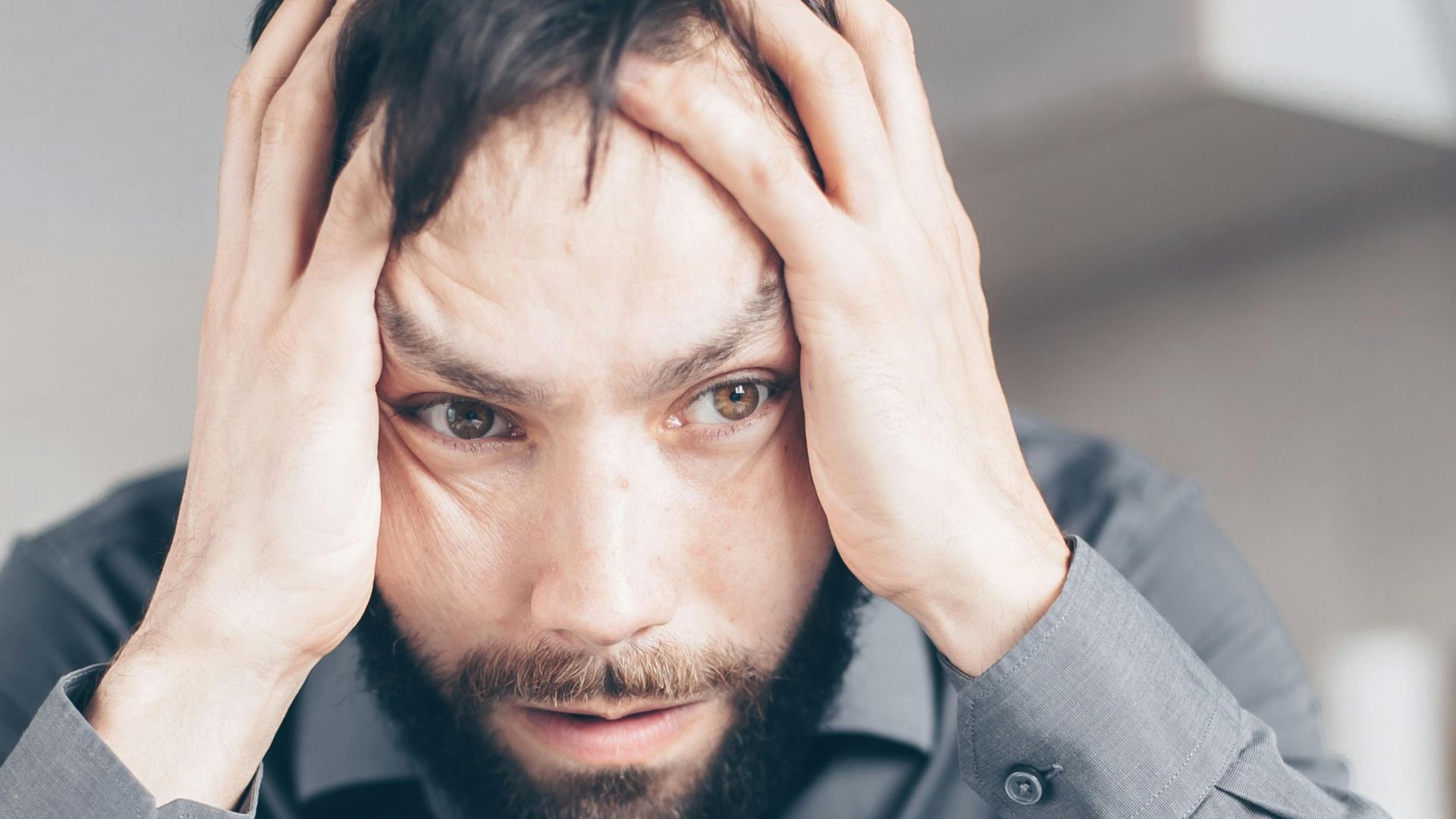 Man with hands on head looking stressed and frustrated indoors.