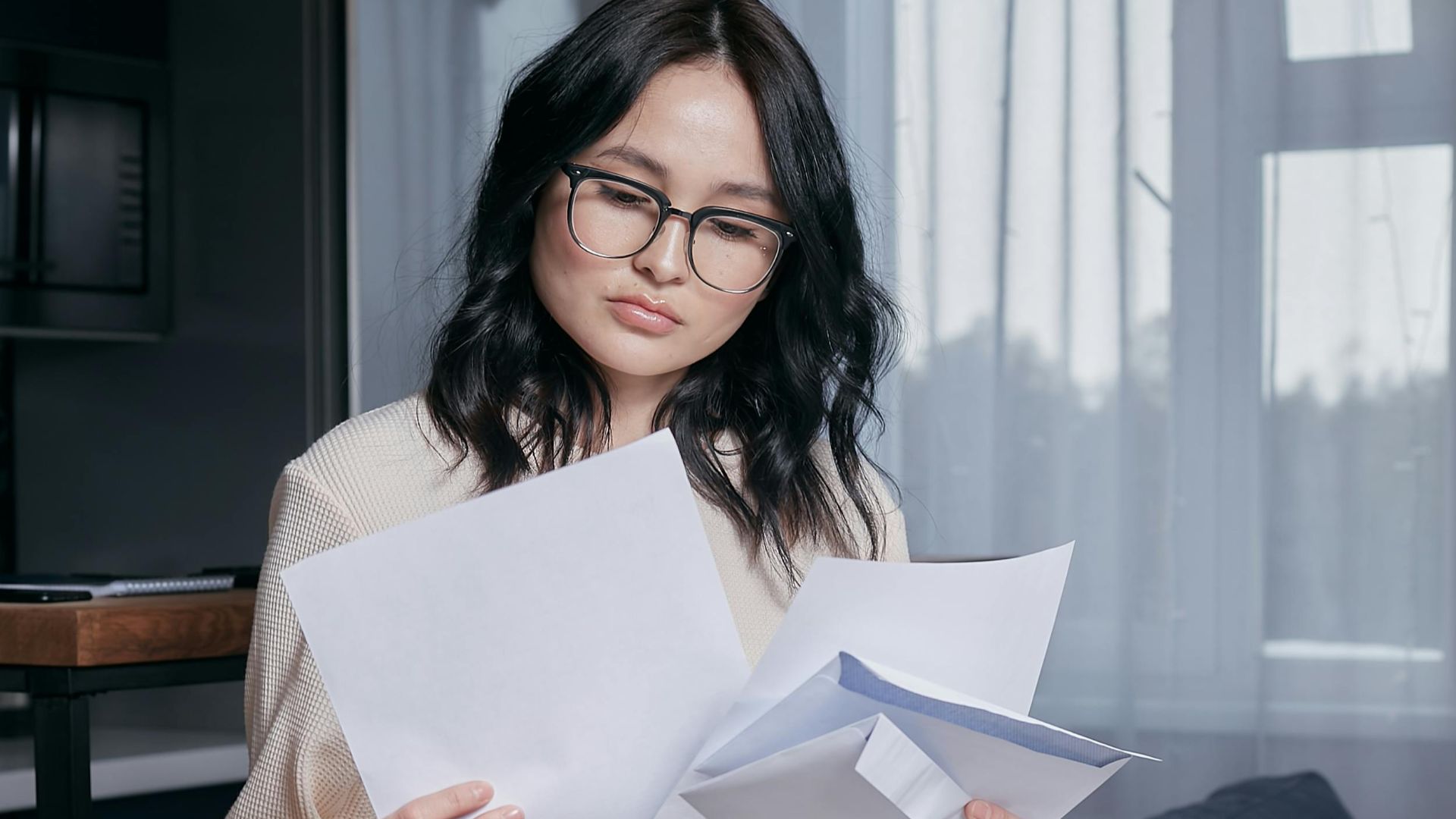 A woman seated indoors carefully reviewing documents, initiating thoughtful analysis.