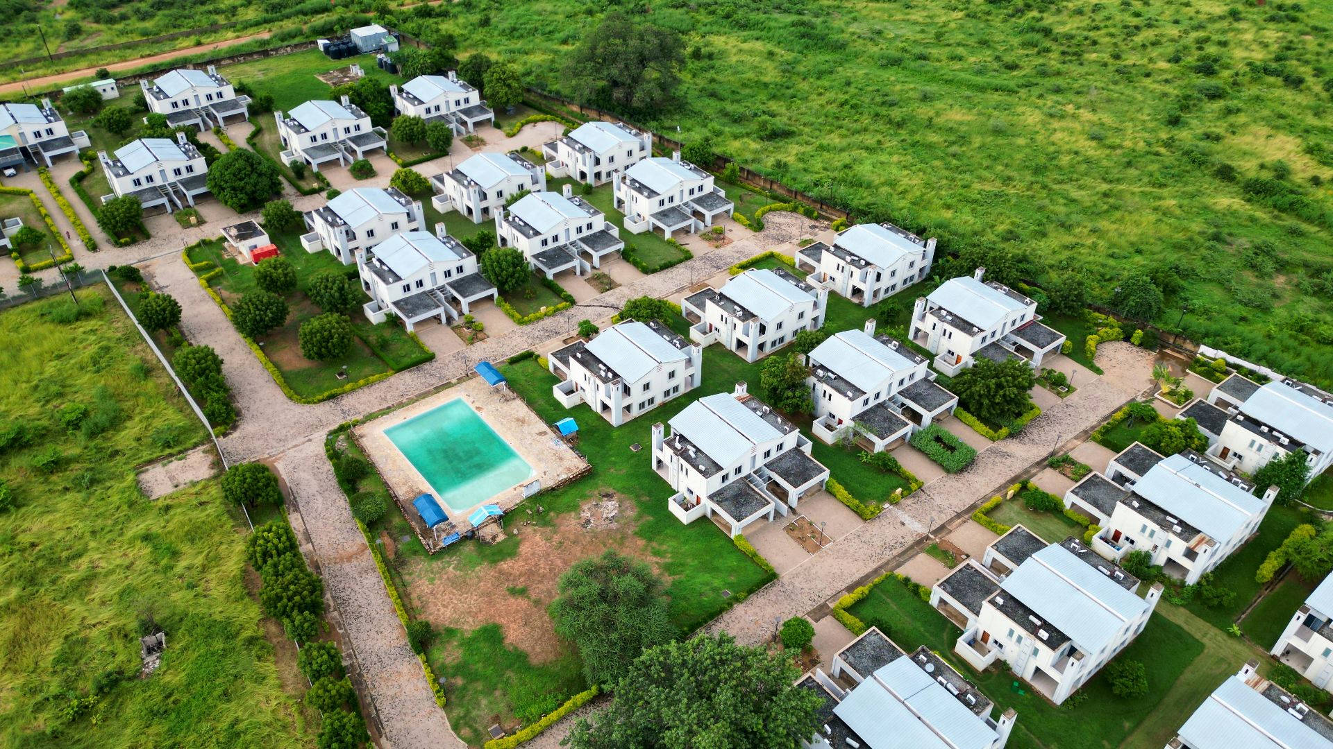 Aerial photograph of a modern housing estate with a communal pool, surrounded by lush greenery.