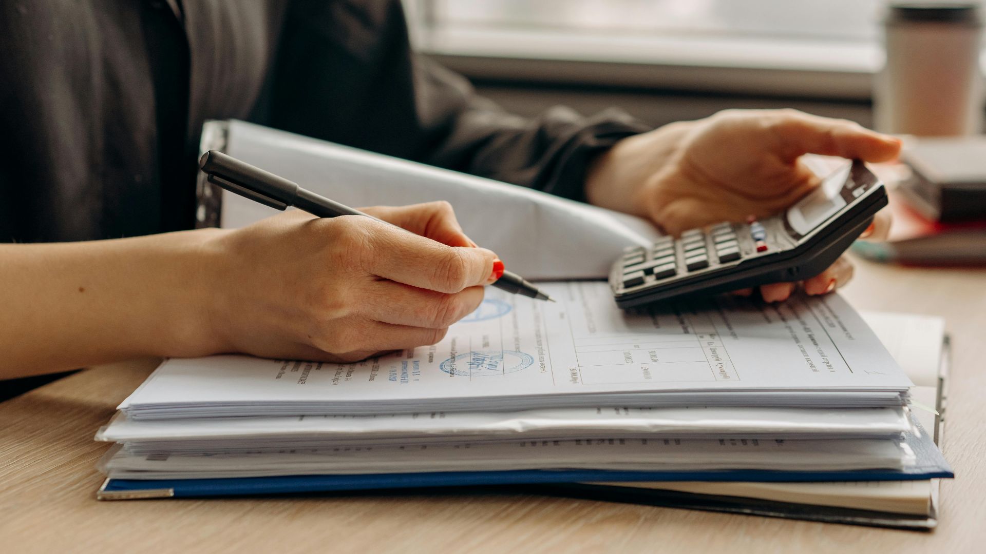 Close-up of person using a calculator with financial documents in an office.