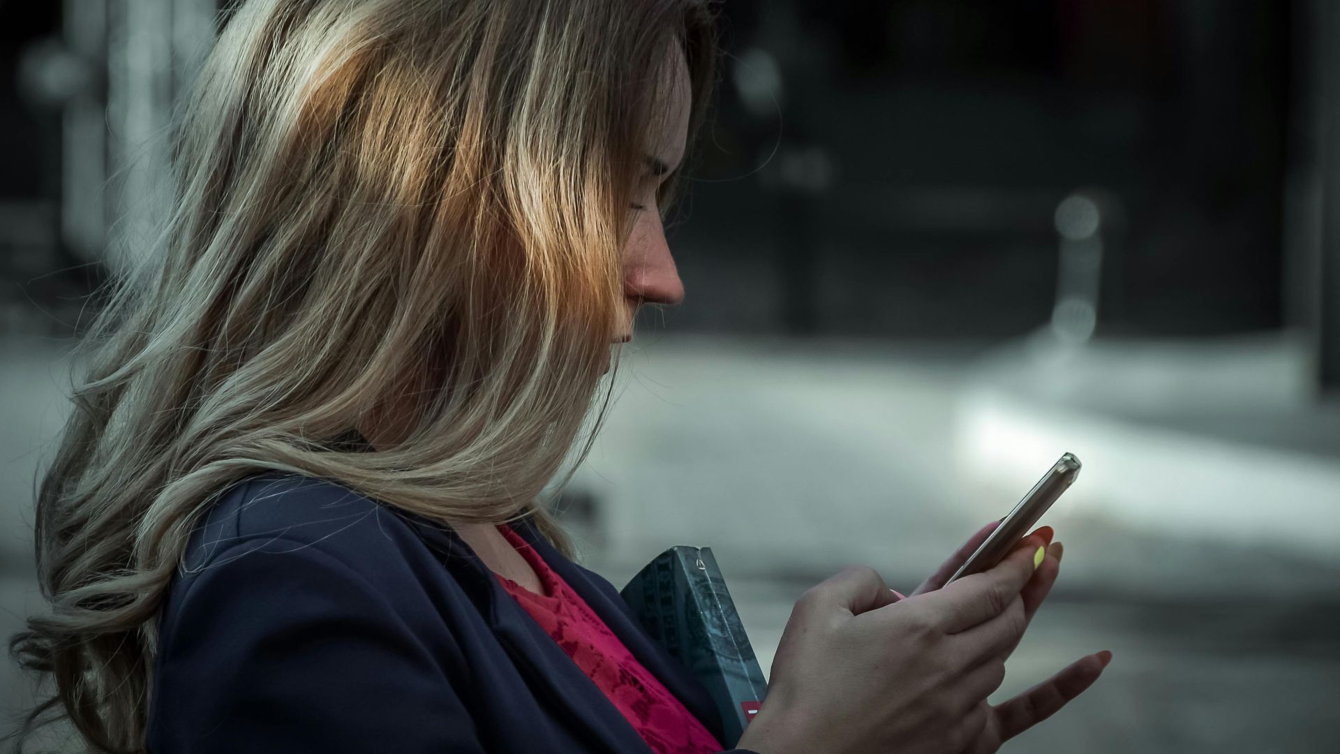 Side profile of a young woman texting on her smartphone in a shaded outdoor area.