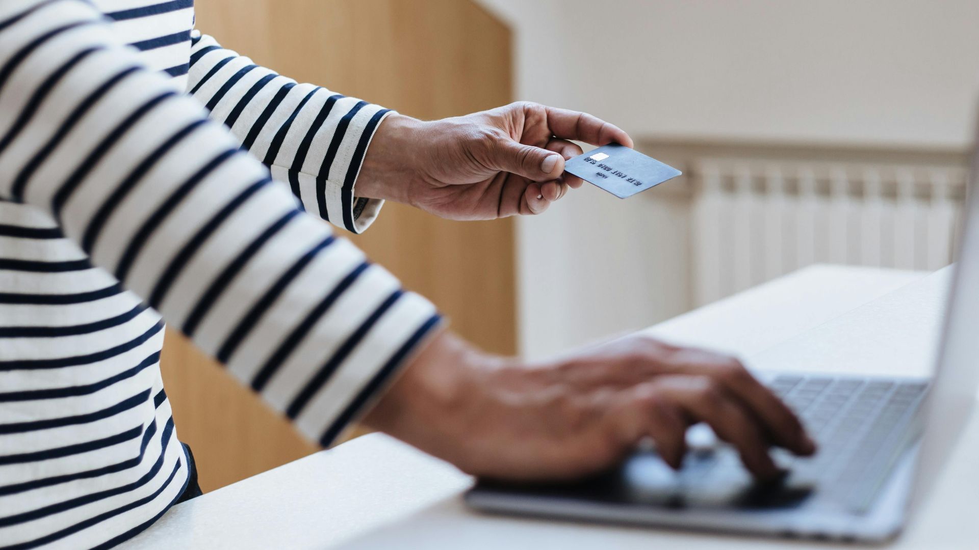 Person using a credit card for online shopping on a laptop indoors.