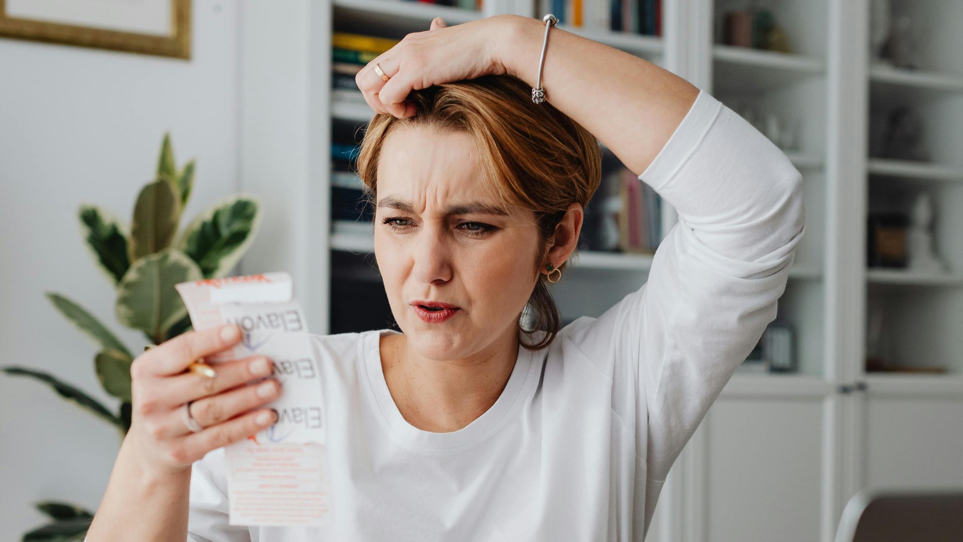 Woman sitting at desk looking stressed while reviewing receipts, depicting financial concern