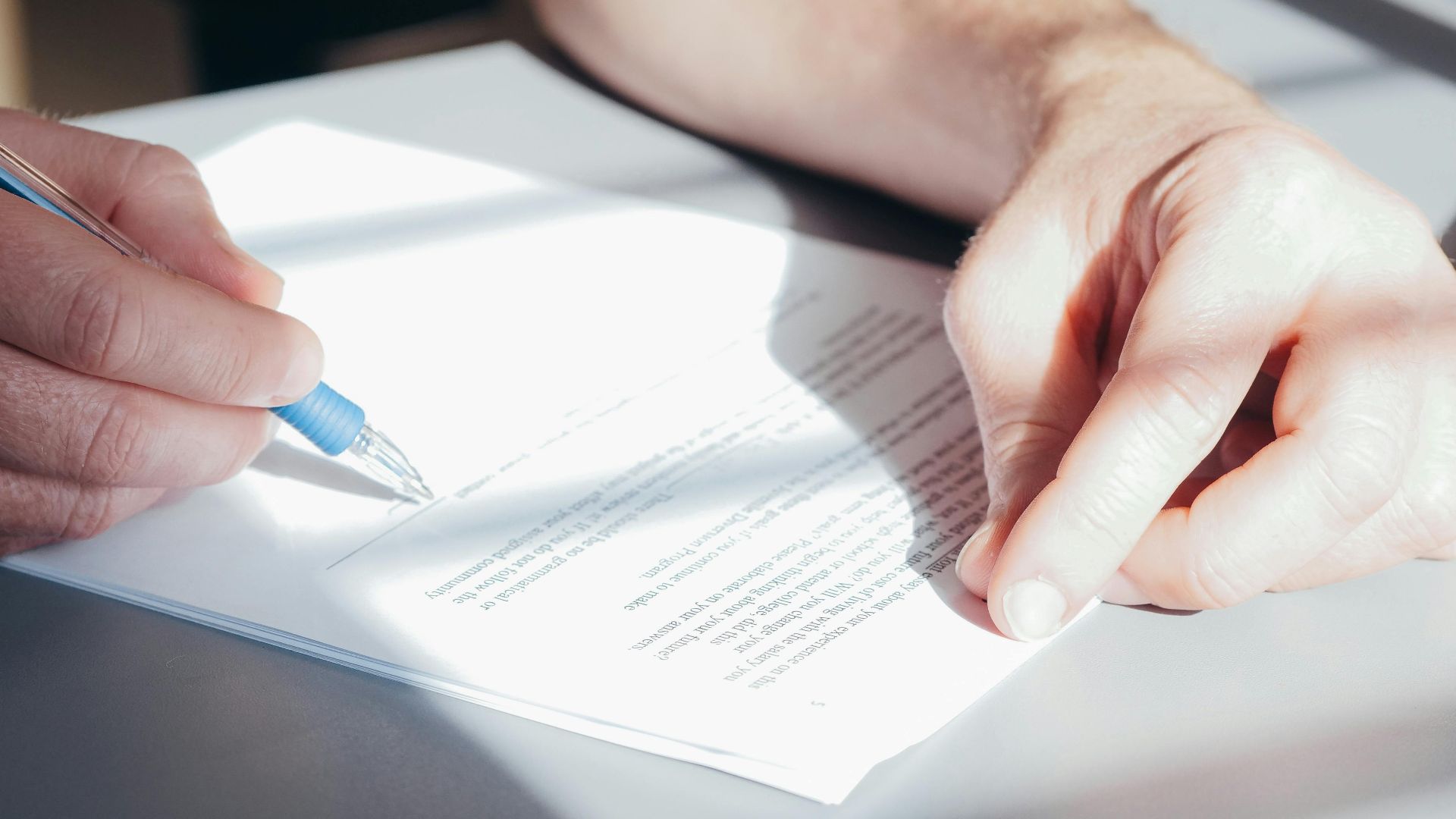 Hands signing a contract with a blue pen, close-up view.