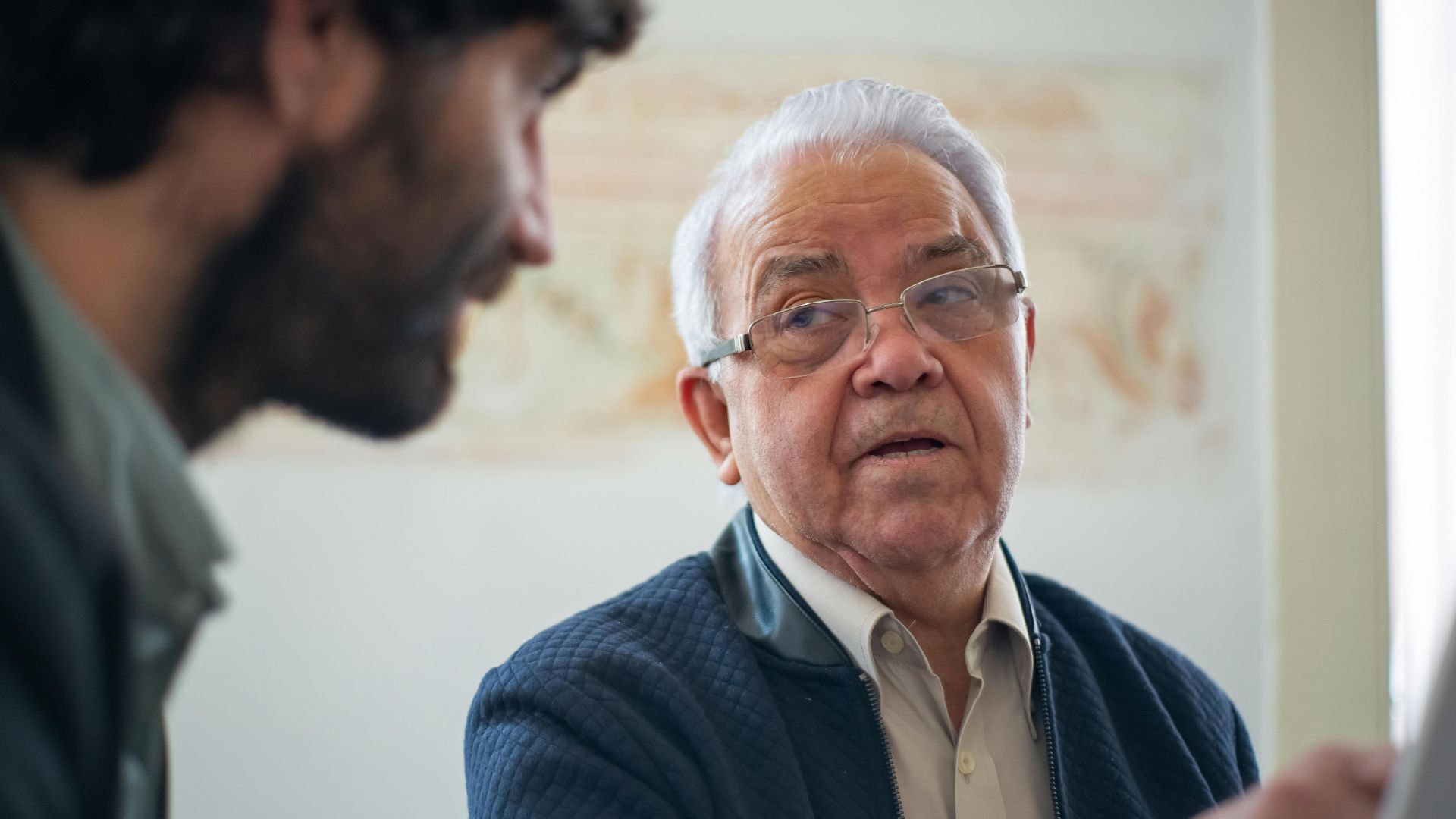 Elderly man with eyeglasses in a thoughtful discussion in Portugal indoors.