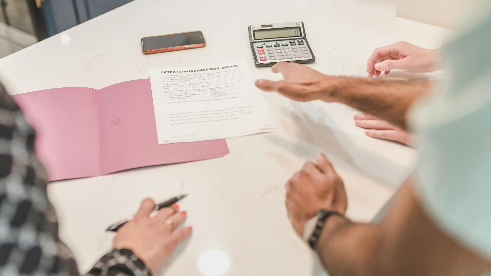Hands gesturing during a real estate document review on a modern office desk with a calculator.