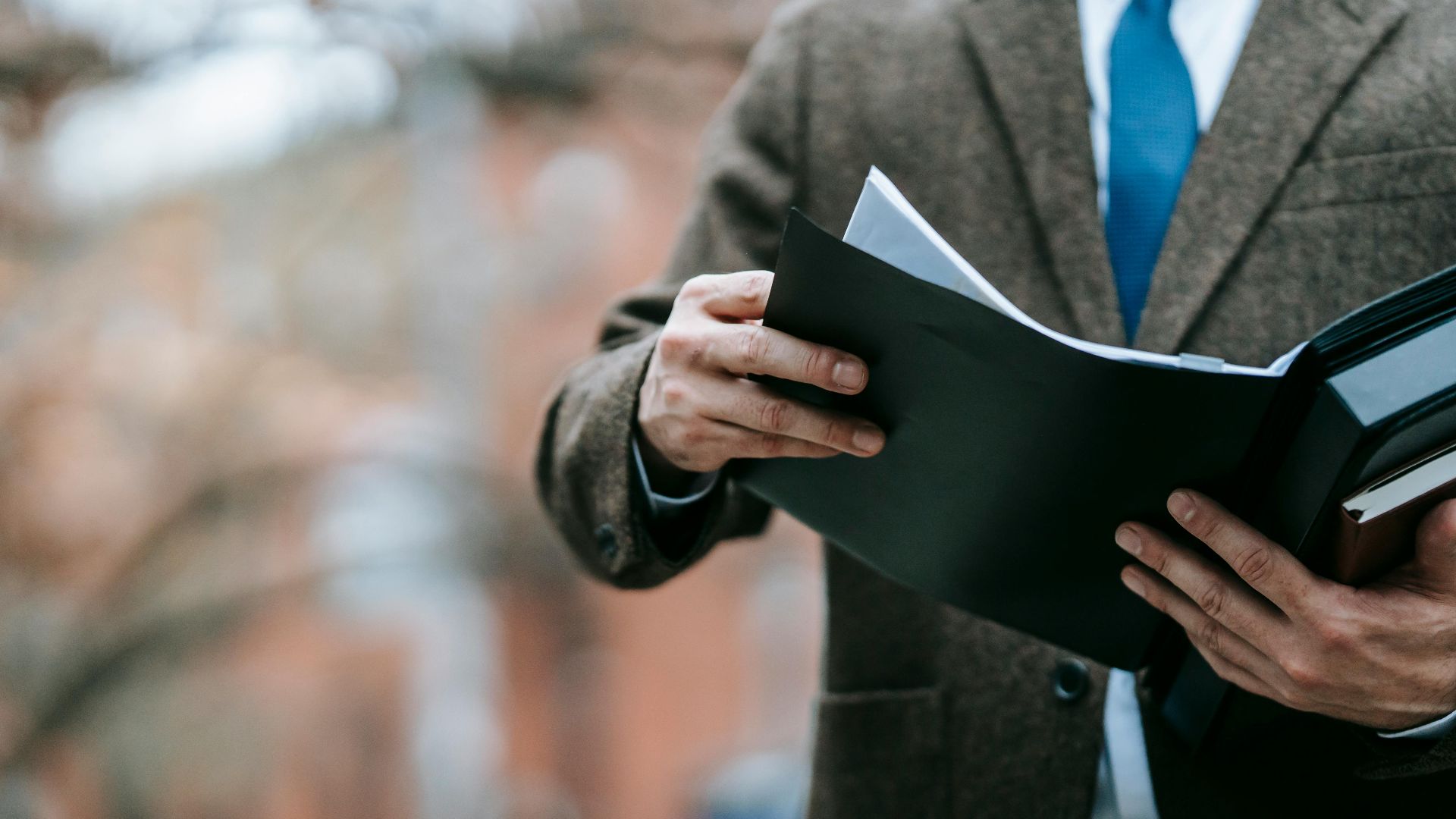 A professional in formal wear reviewing documents outside, showcasing business attire and focus.