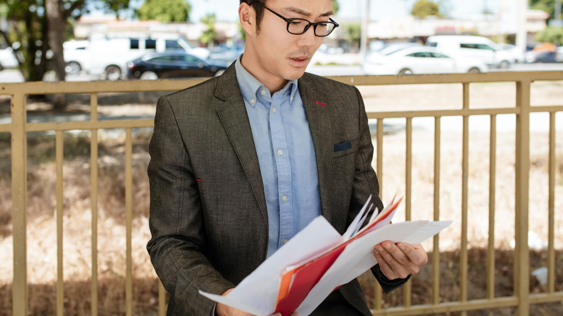 Asian businessman in a suit checking documents outdoors on a sunny day.