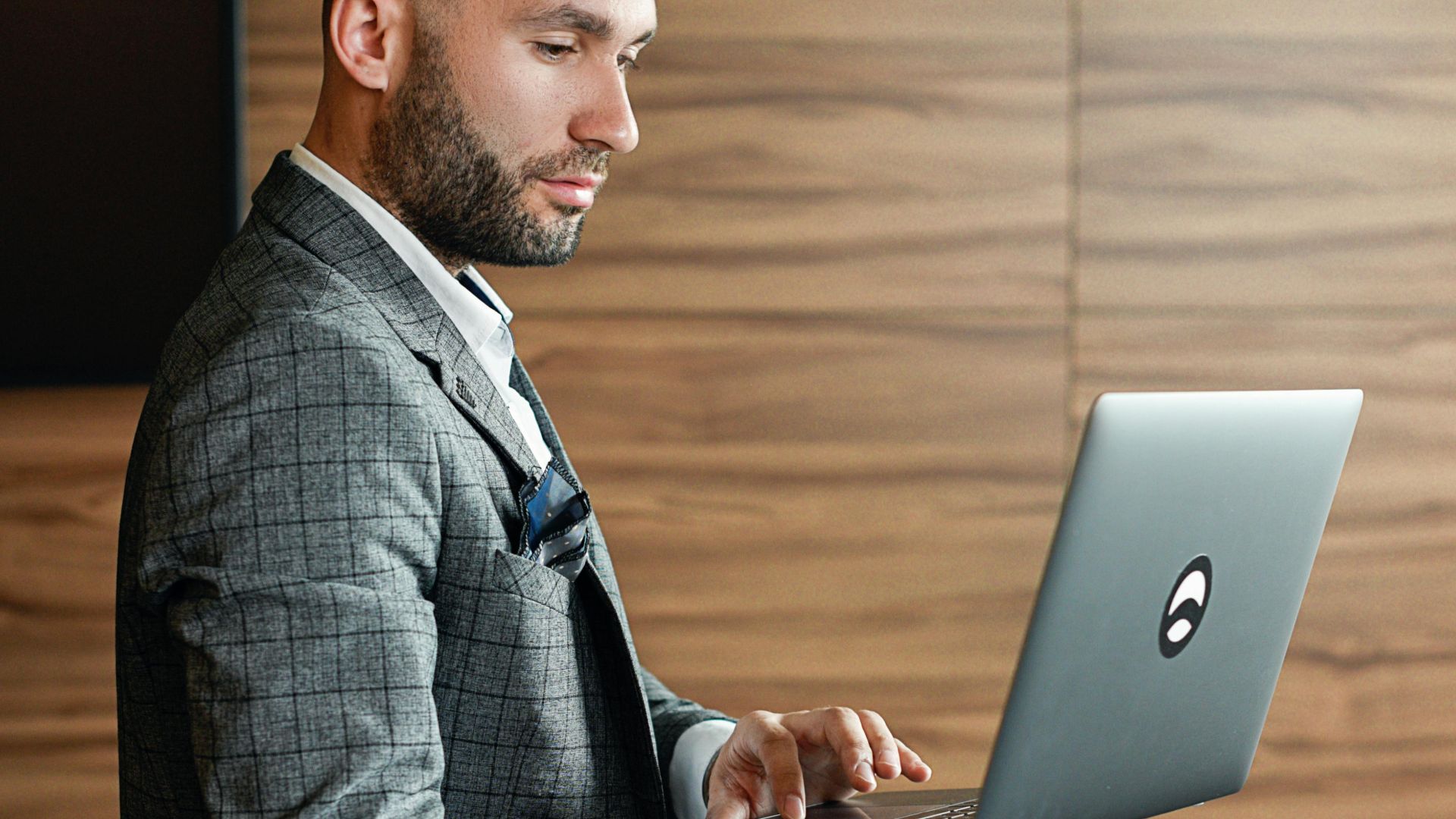 Side view of a businessman with facial hair using a laptop while leaning on a table indoors.