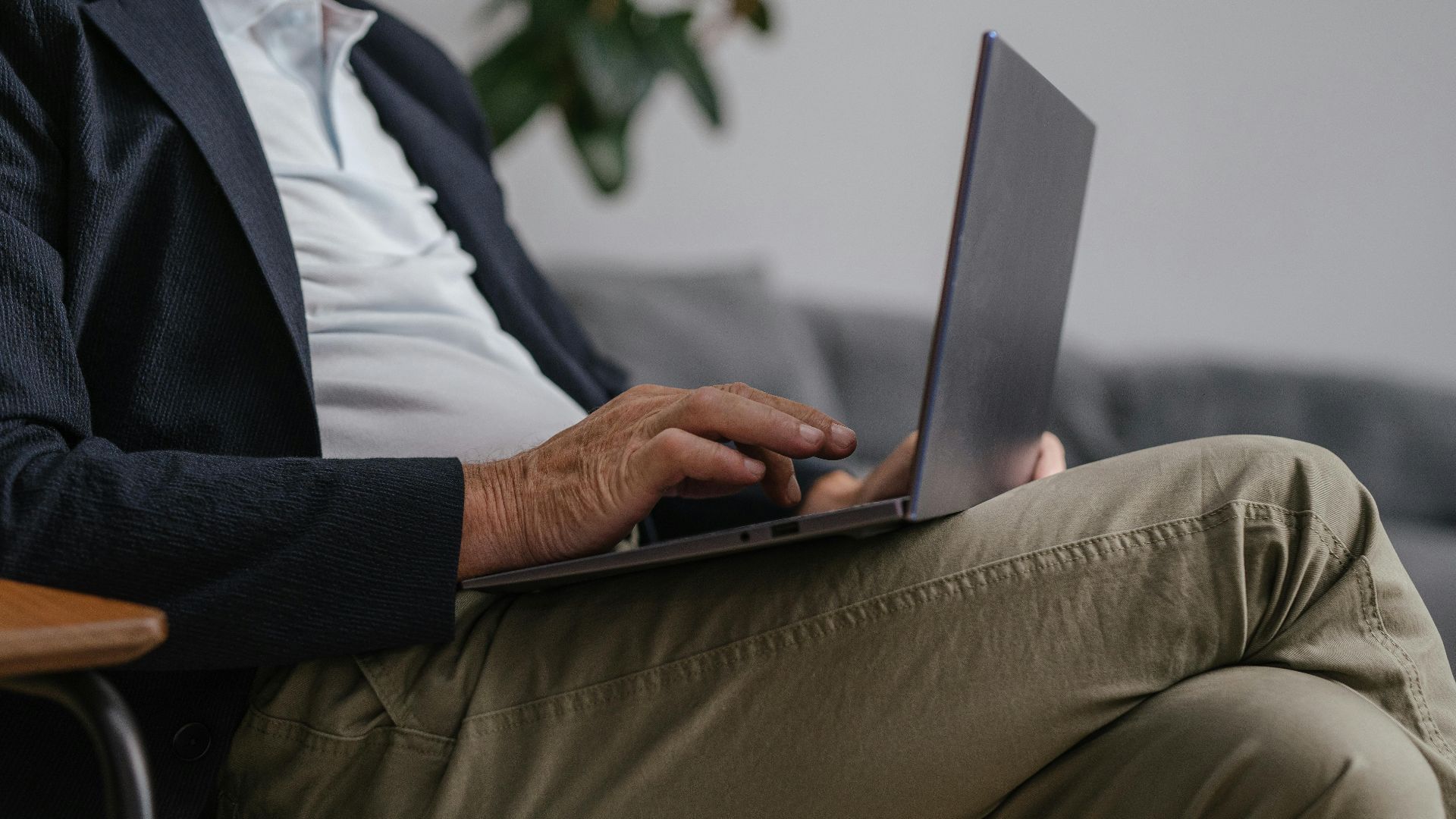 Close-up of a man in a suit jacket using a laptop indoors, showcasing a relaxed work environment.