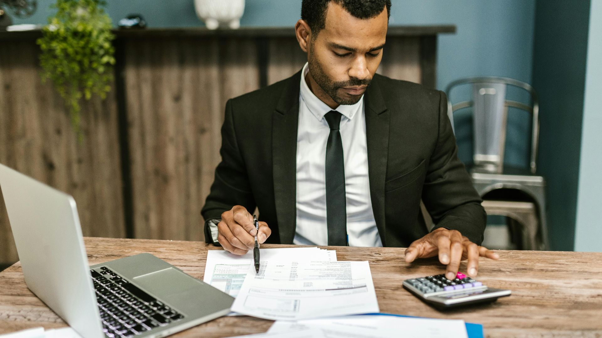 A focused businessman works with a calculator and documents in a modern office.
