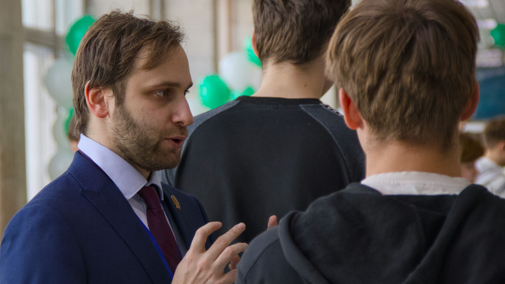 A man in a suit talks to two young men.
