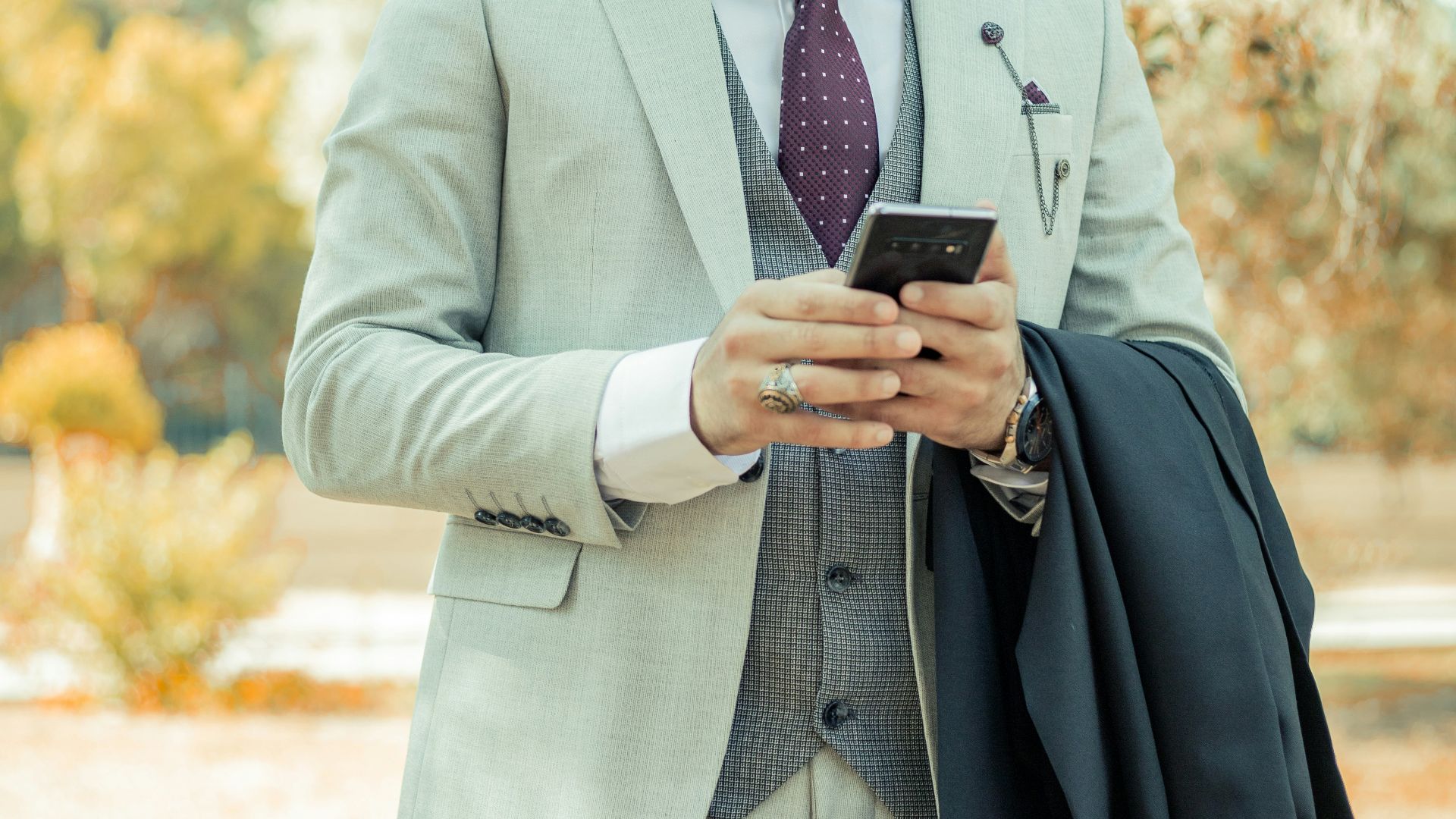 man in gray suit jacket holding black smartphone