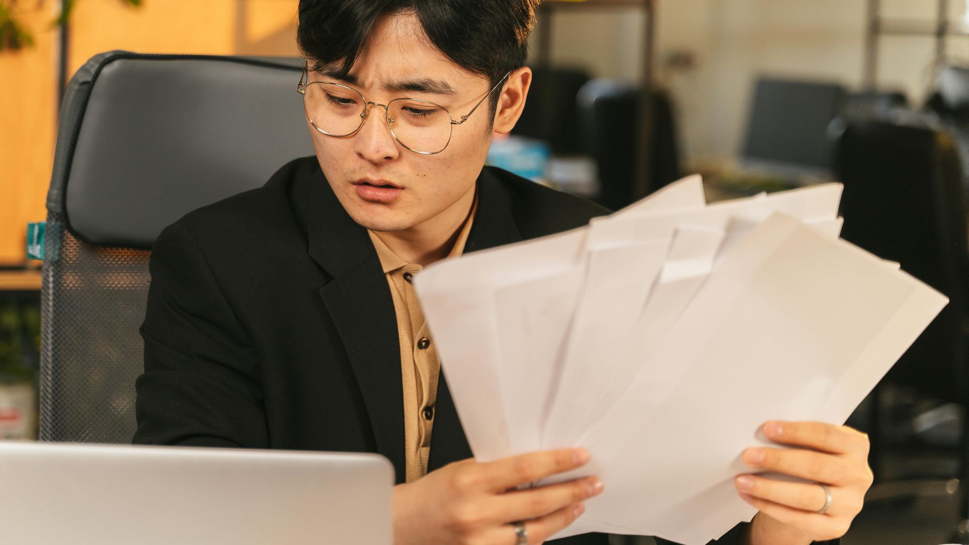 Businessman in glasses reviewing paperwork in a modern office setting.