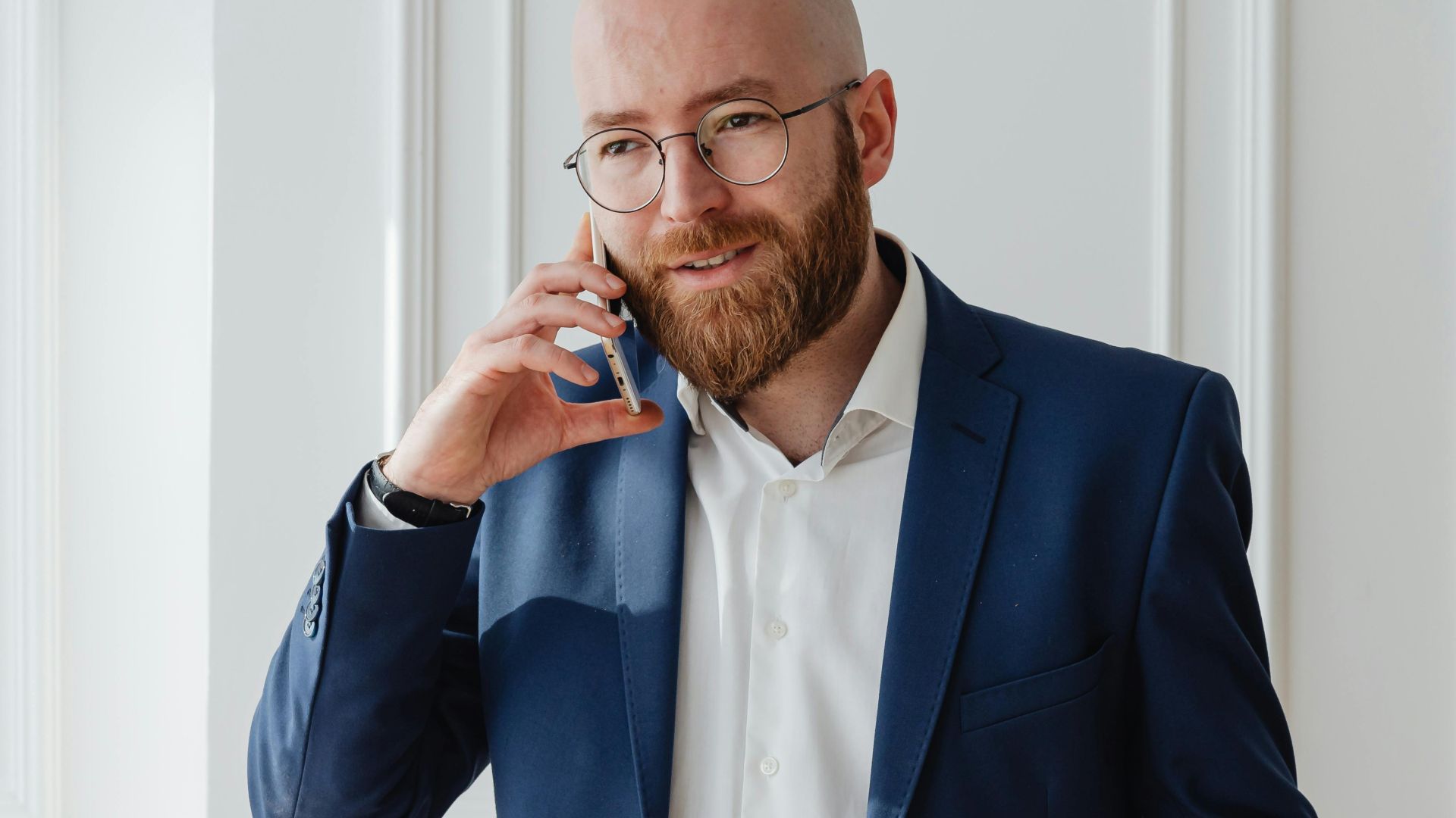 Bald bearded businessman in a suit having a phone call indoors.